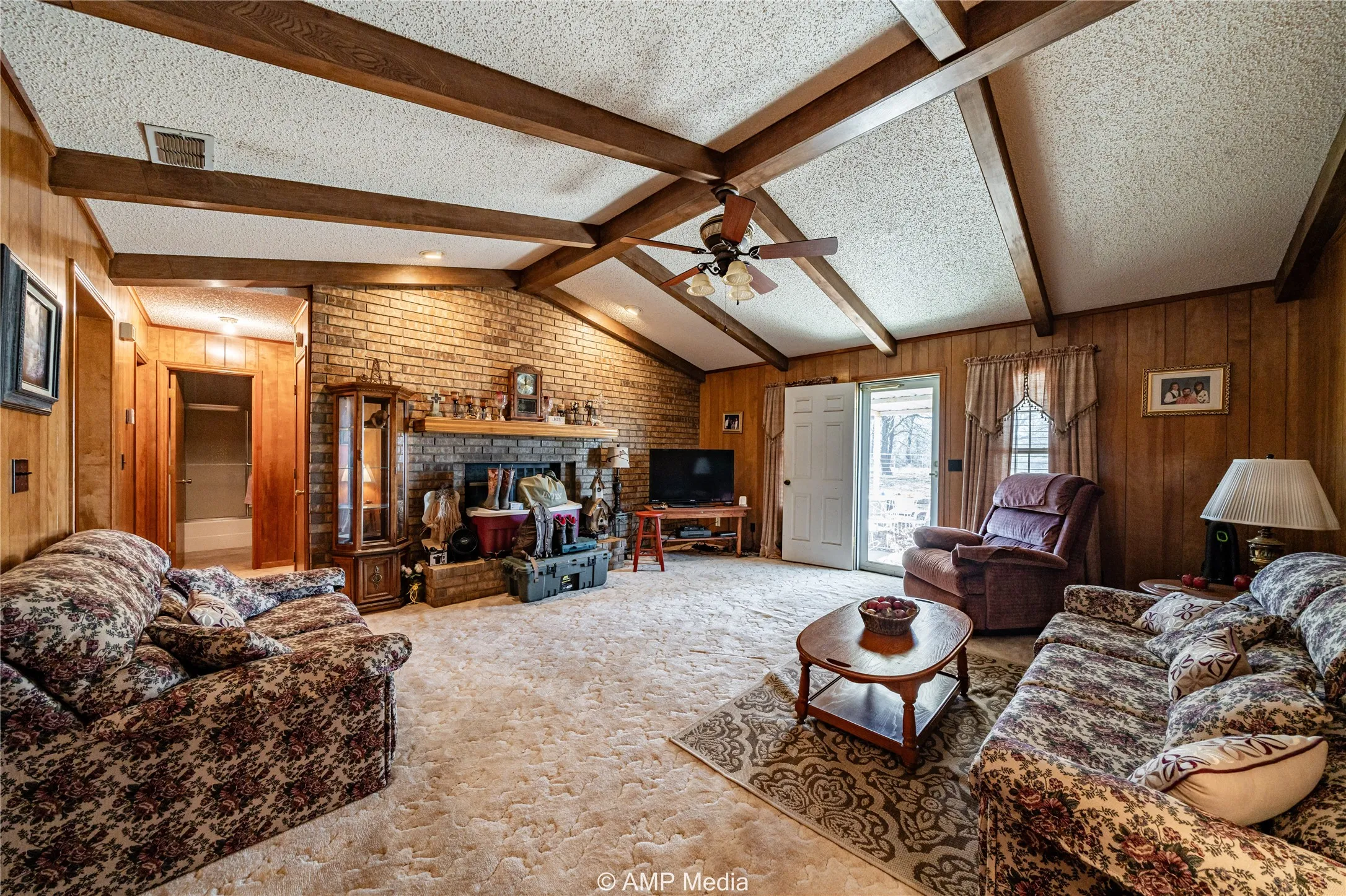 Carpeted living room featuring a fireplace, wooden walls, a textured ceiling, and vaulted ceiling with beams