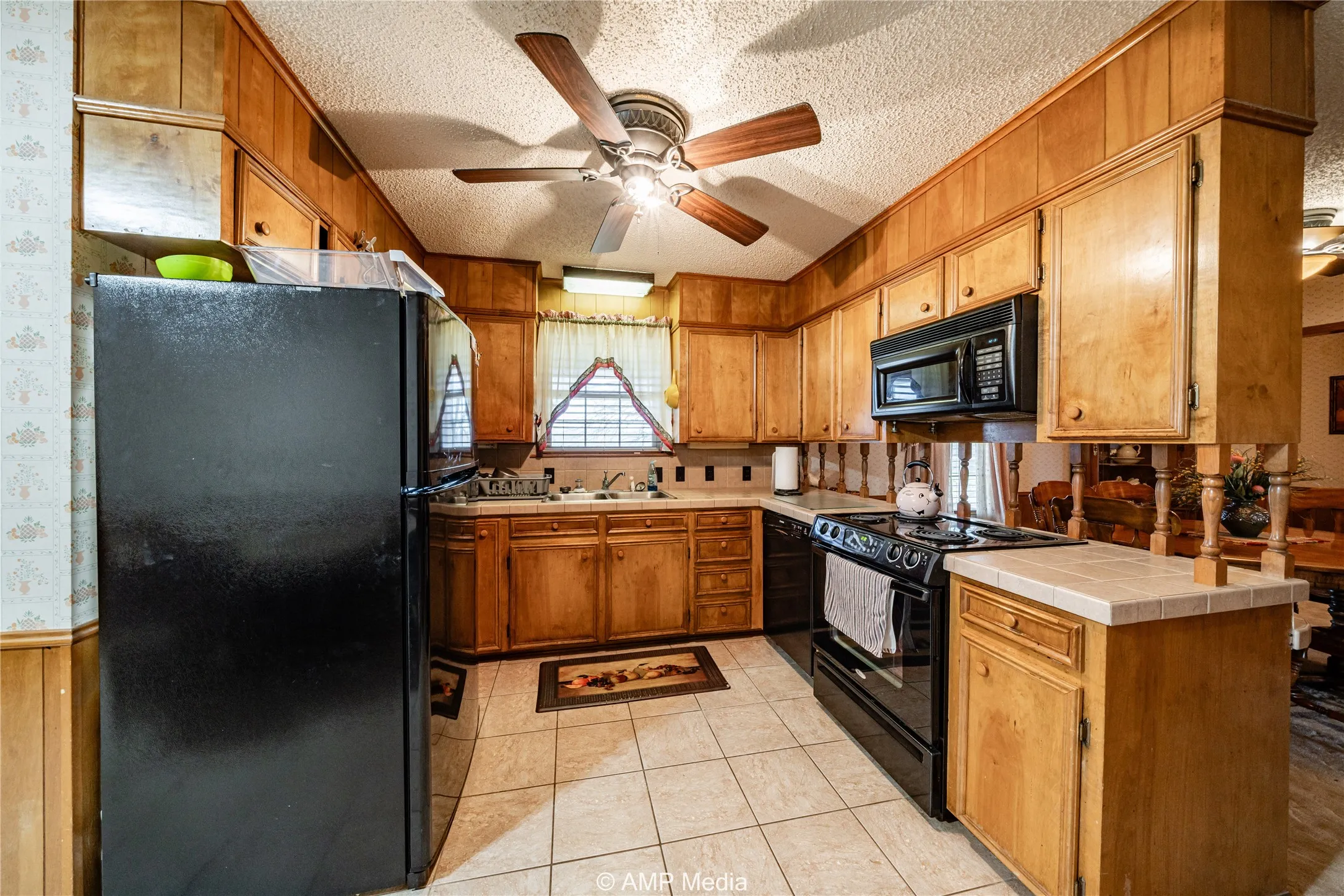 Kitchen with sink, light tile patterned floors, tile counters, black appliances, and a textured ceiling