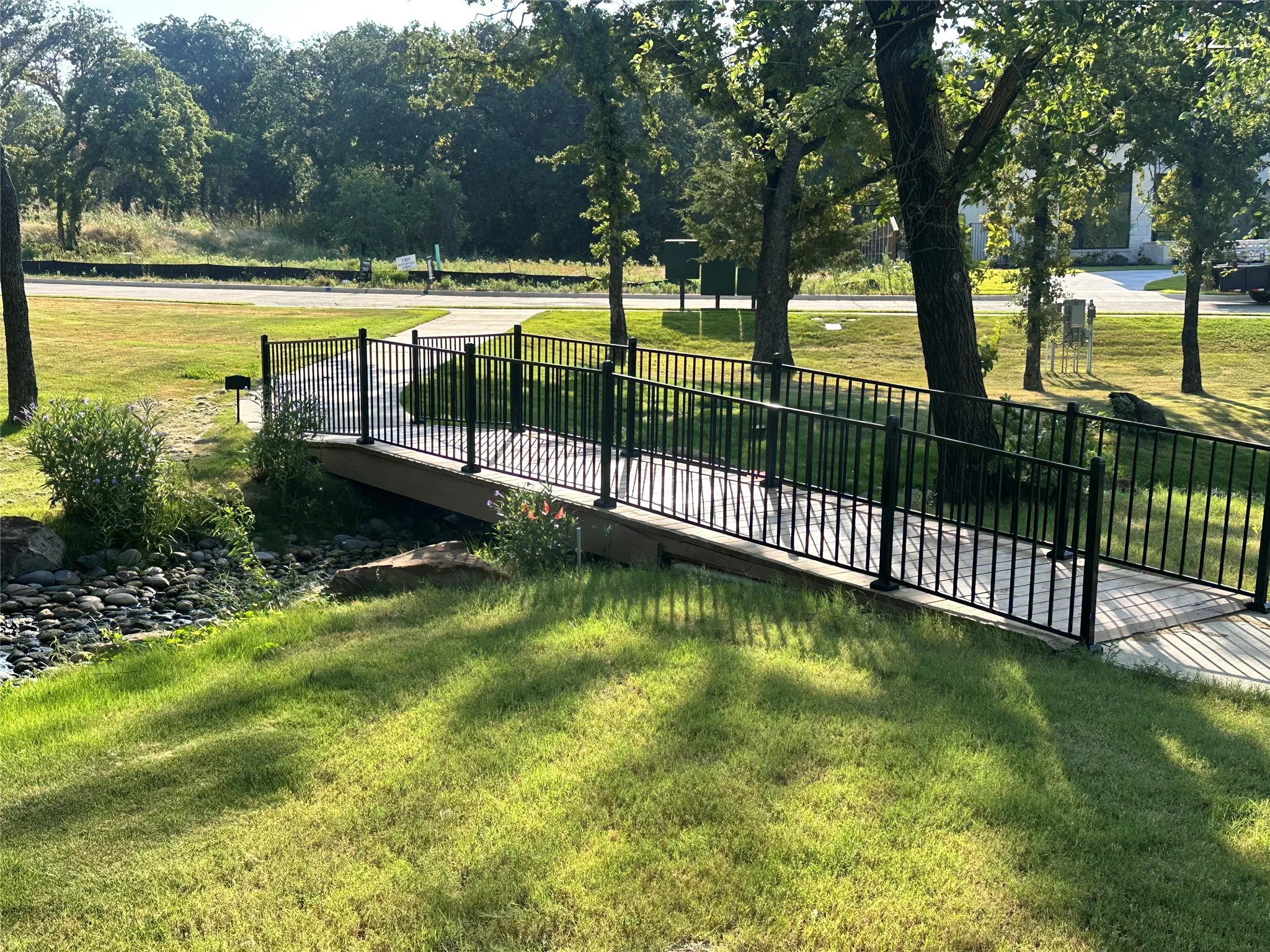 Pedestrian bridge with black metal railings, crossing a rocky creek bed