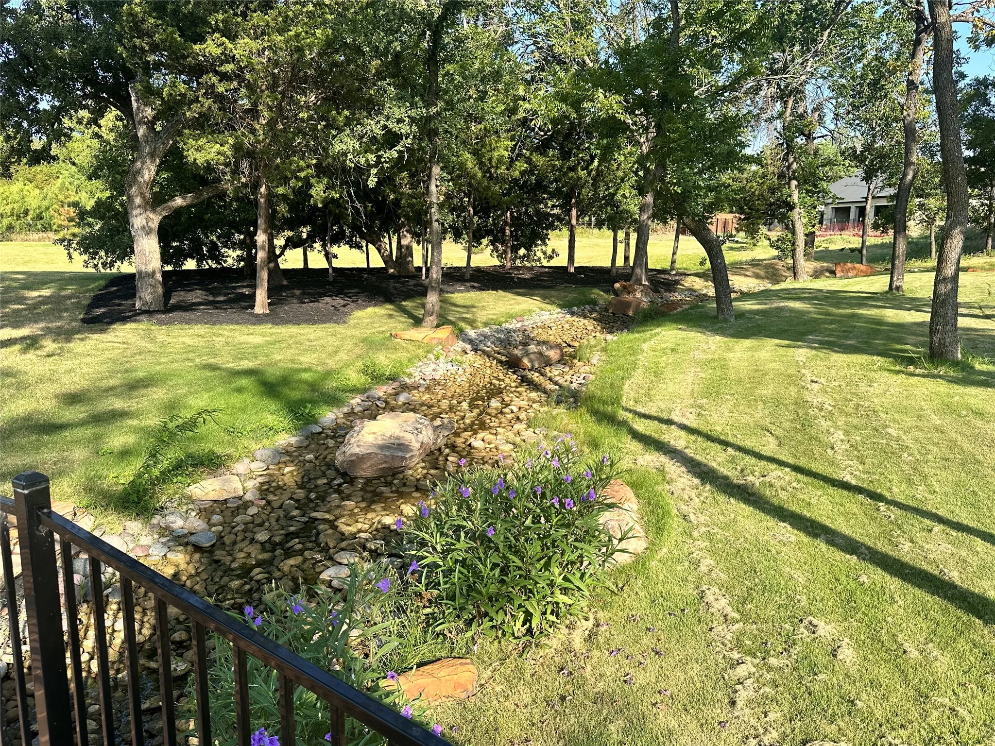 Expansive lawn with mature trees, a creek bed featuring natural stone accents, and ornamental plantings
