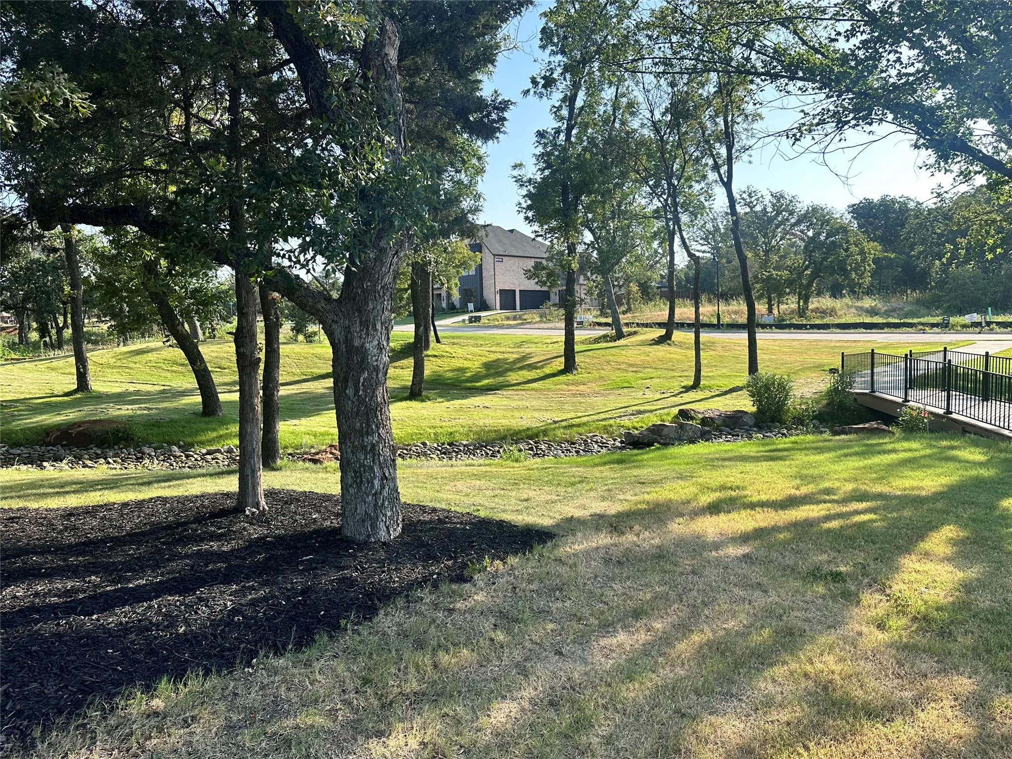 Manicured green spaces featuring mature trees and a pedestrian bridge with black railings