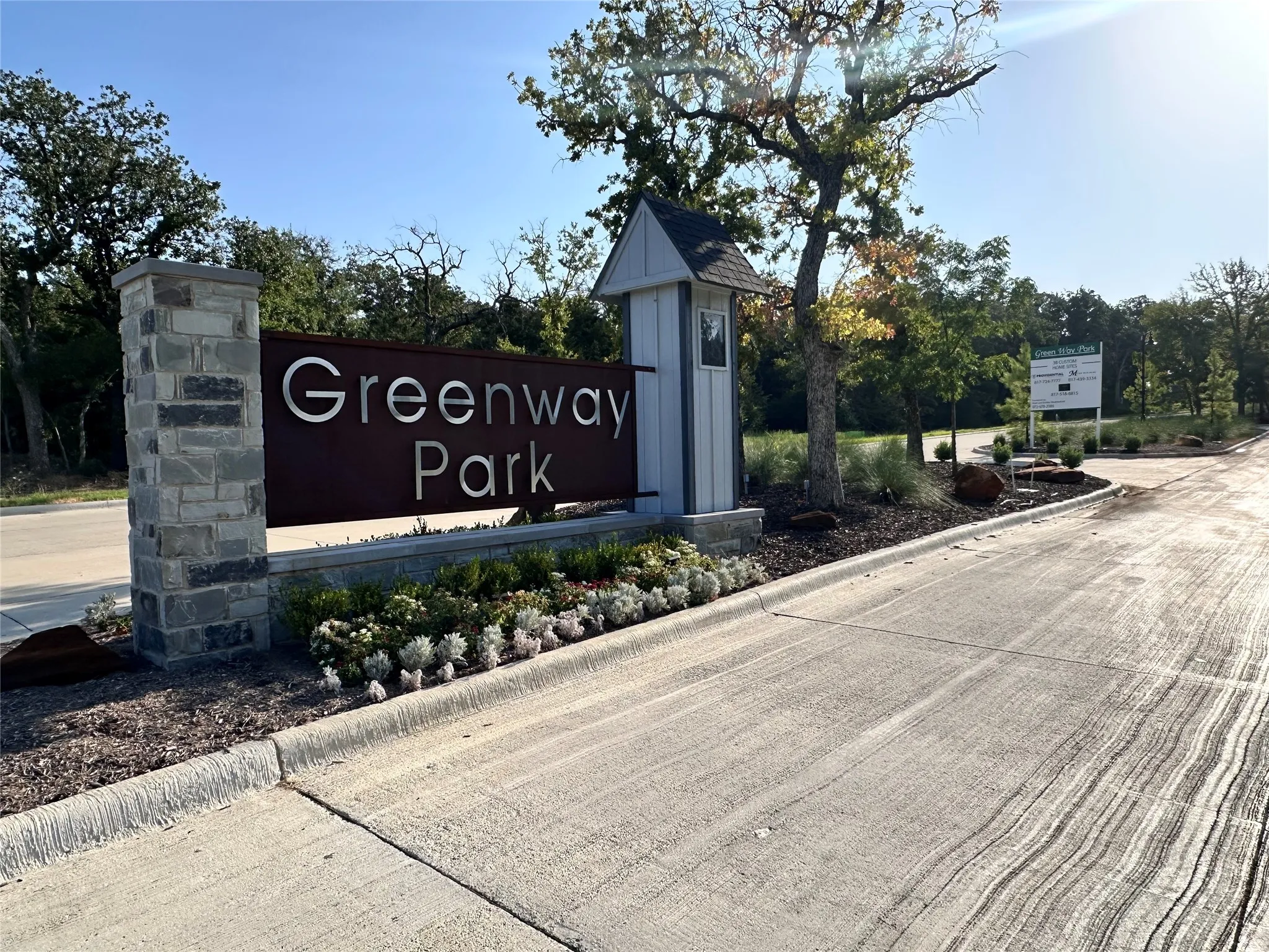 Stone and metal entrance signage, mature tree landscaping, and concrete road surfacing