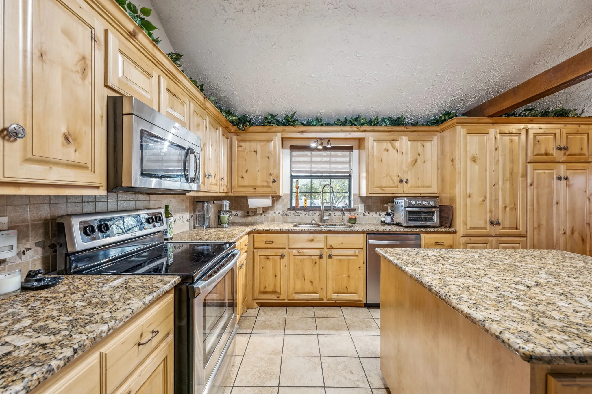 Kitchen featuring light tile patterned floors, appliances with stainless steel finishes, a sink, and light stone countertops