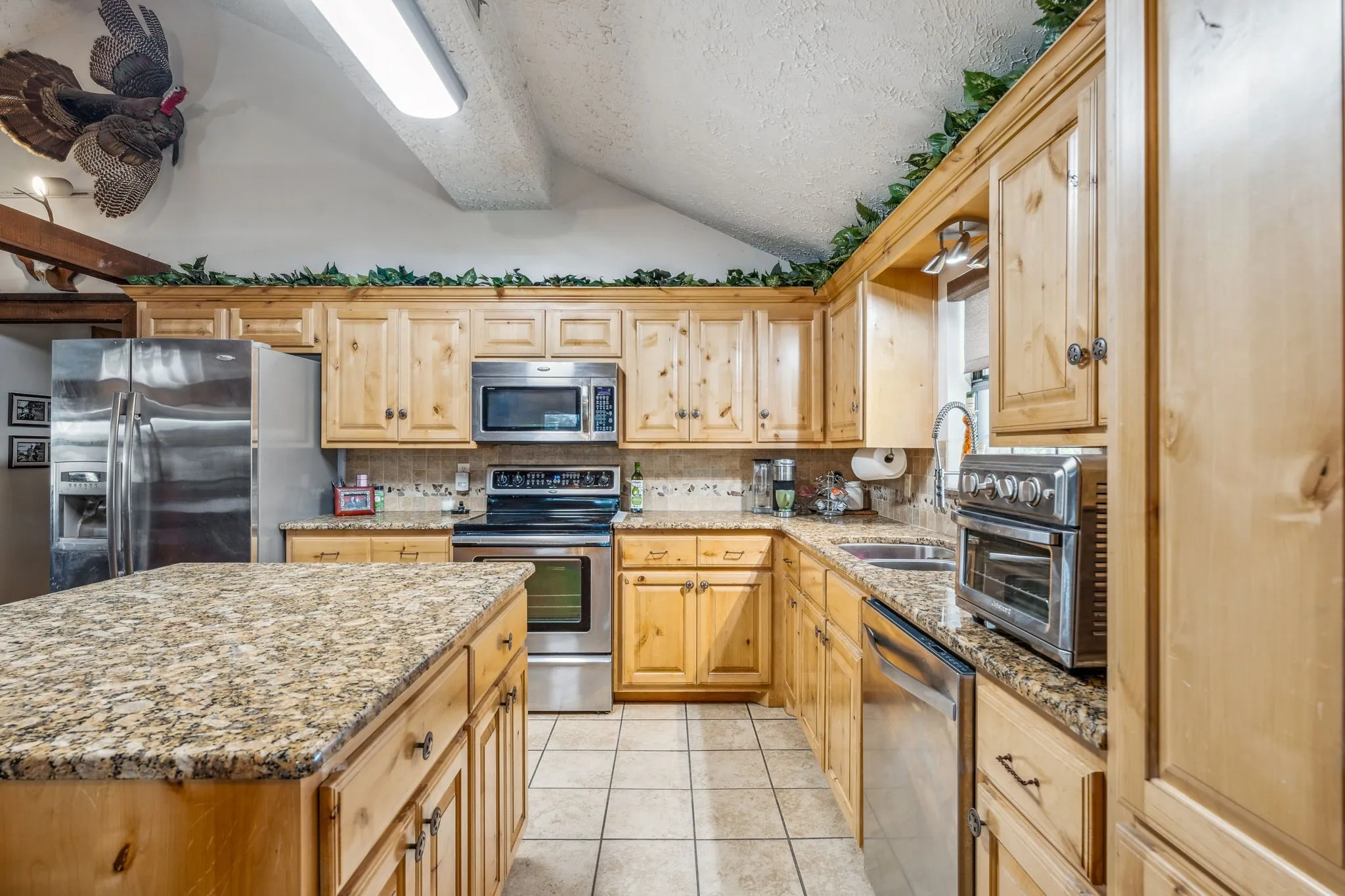 Kitchen featuring light tile patterned floors, stainless steel appliances, lofted ceiling, decorative backsplash, and a sink