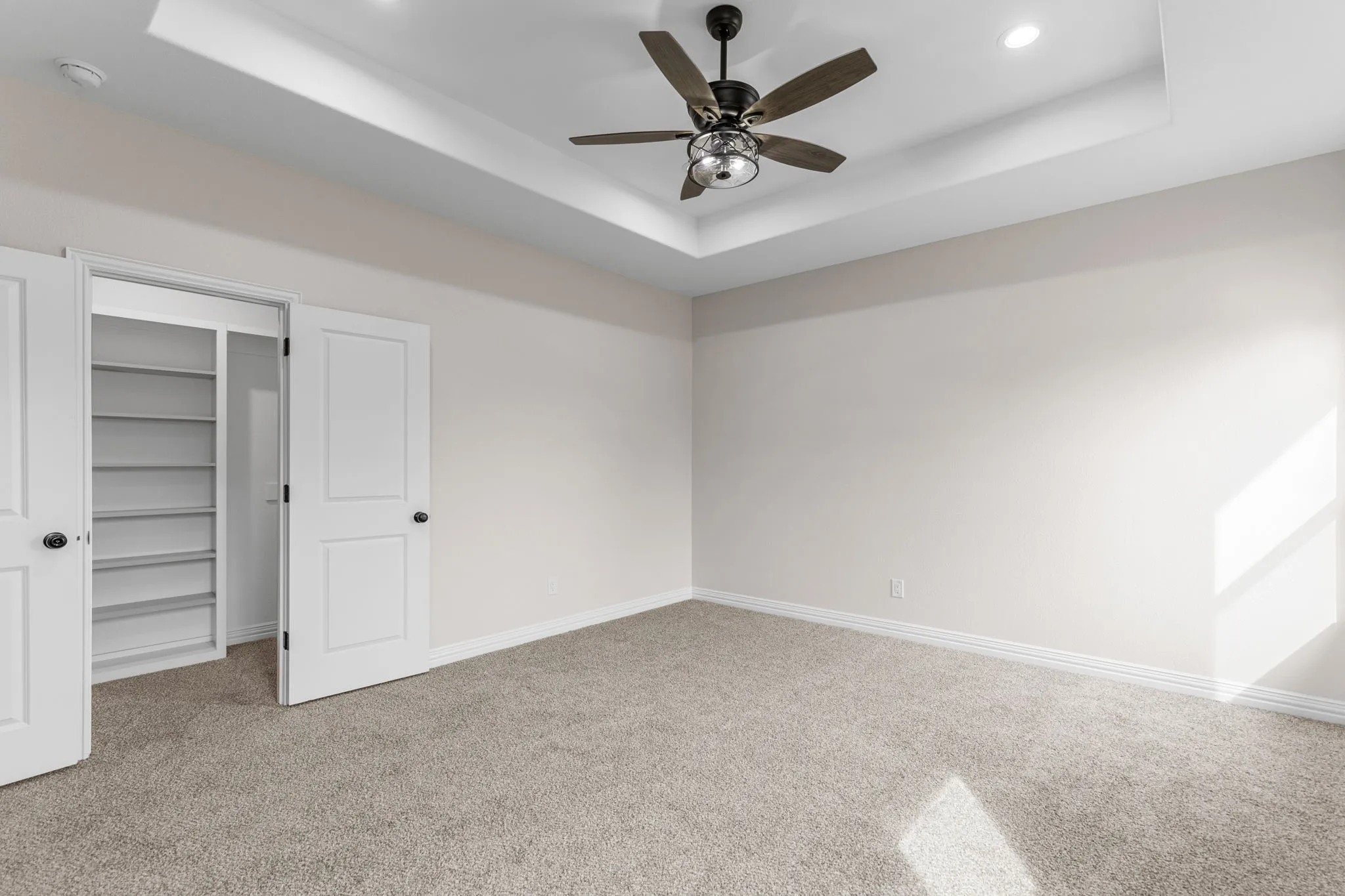 Unfurnished bedroom featuring carpet floors, a walk in closet, ceiling fan, a raised ceiling, and a closet