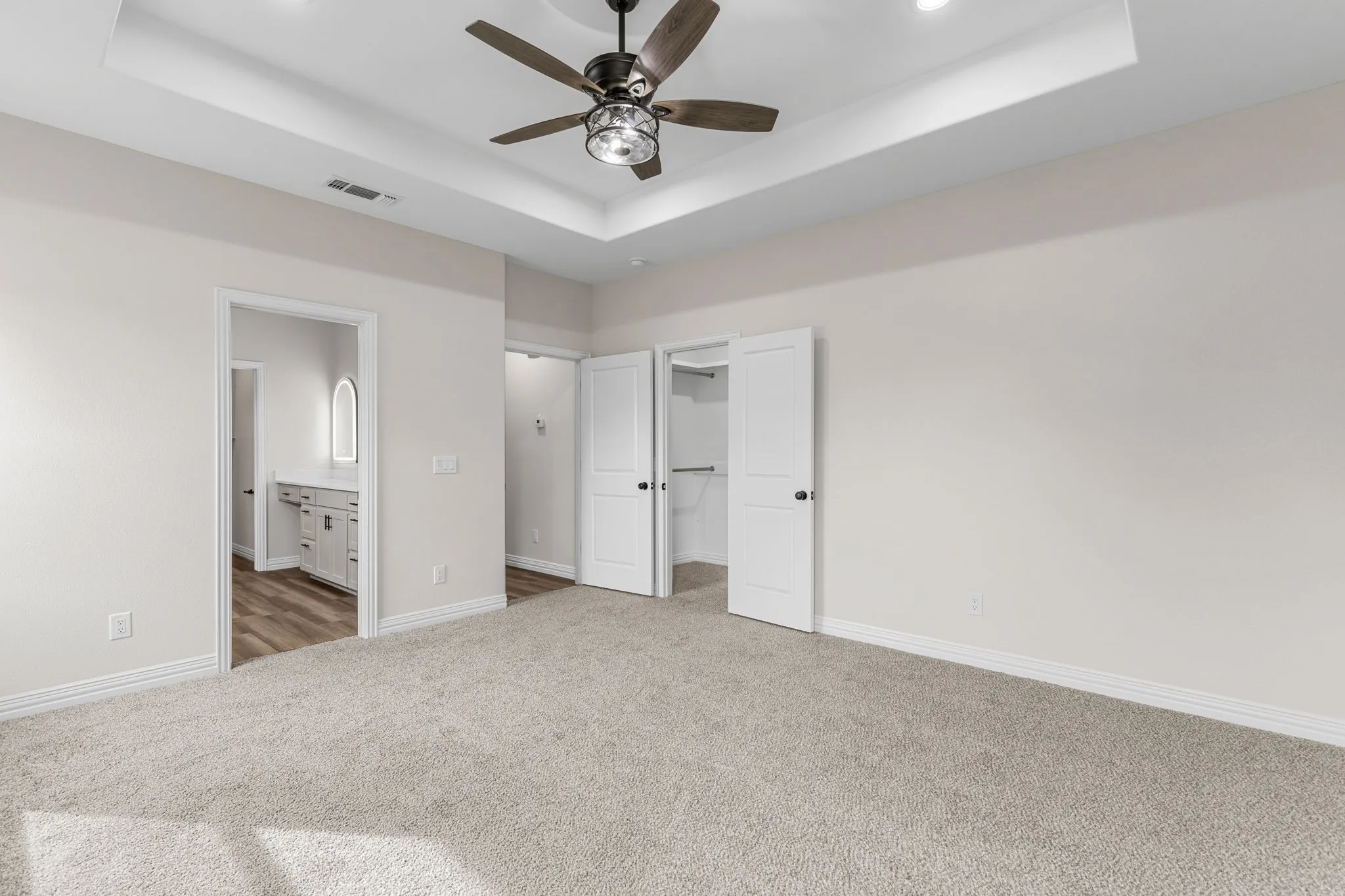Unfurnished bedroom featuring a raised ceiling, dark colored carpet, a spacious closet, and ensuite bath