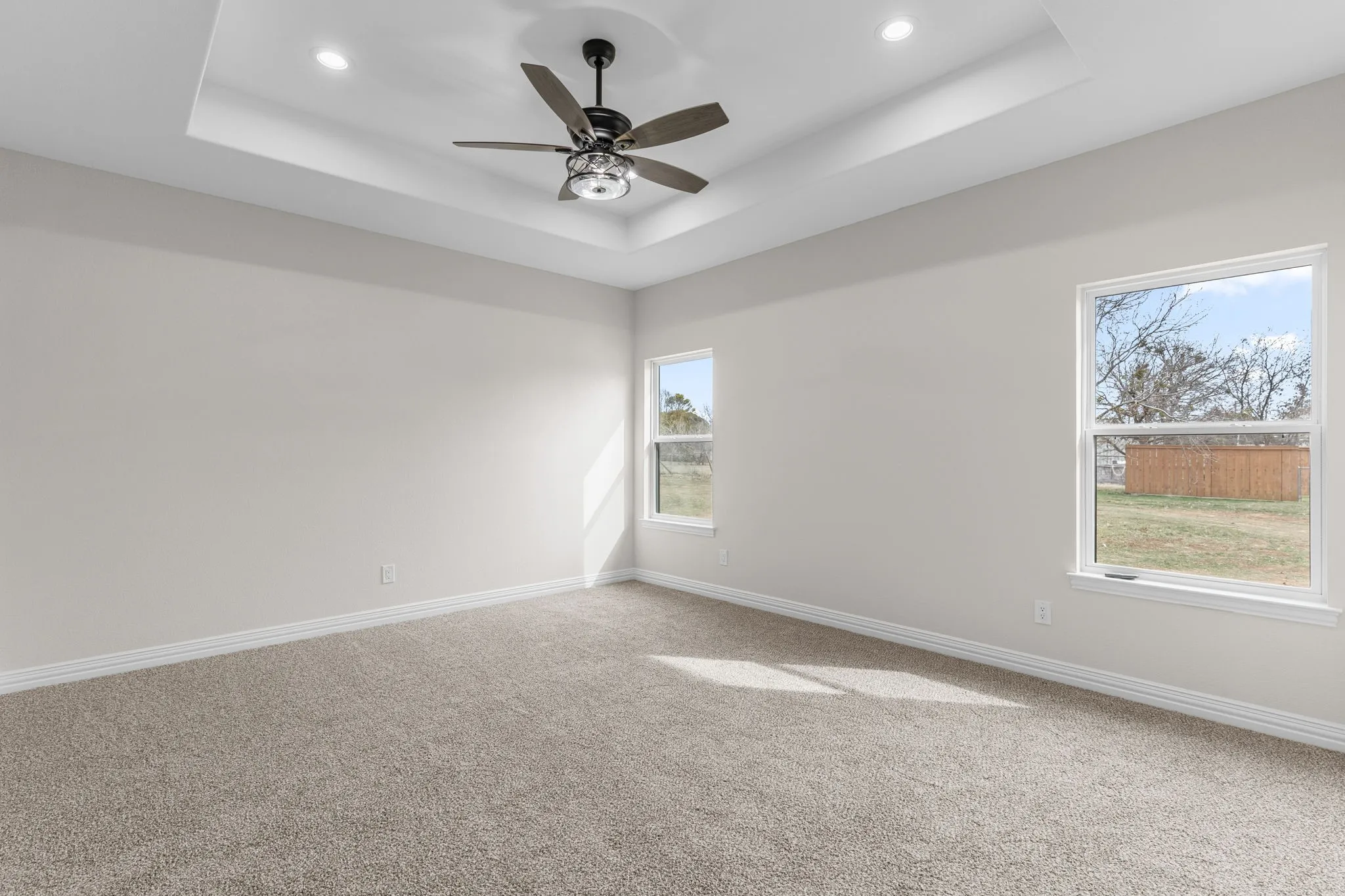 Carpeted empty room featuring ceiling fan and a tray ceiling