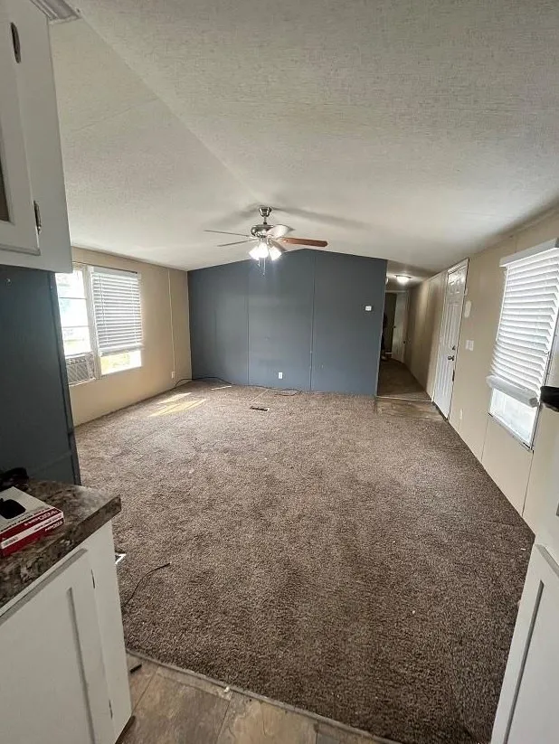 Unfurnished living room featuring light colored carpet, a textured ceiling, and ceiling fan