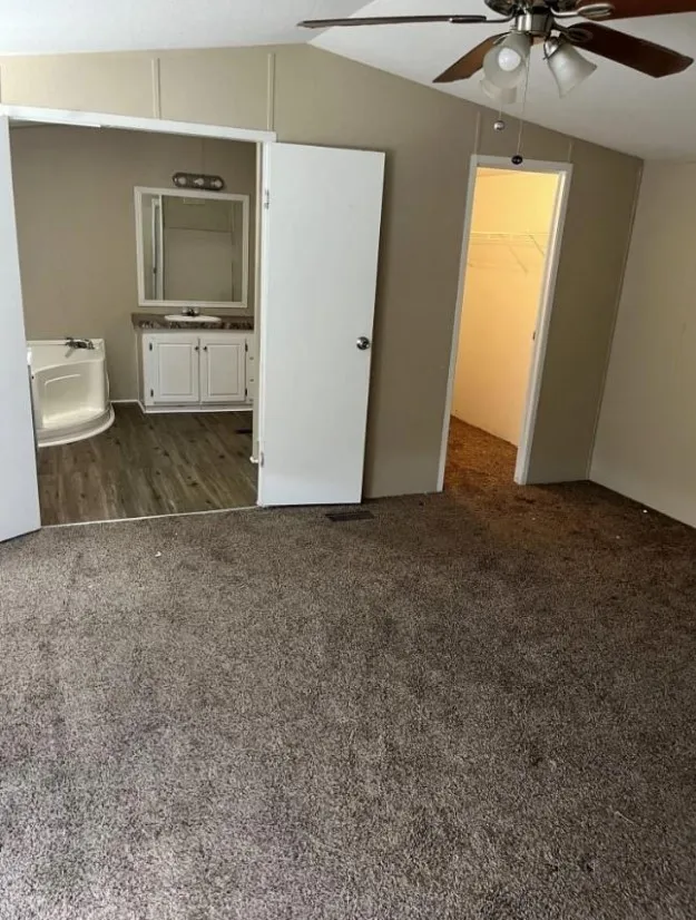 Unfurnished bedroom with a closet, a spacious closet, ceiling fan, vaulted ceiling, and dark carpet