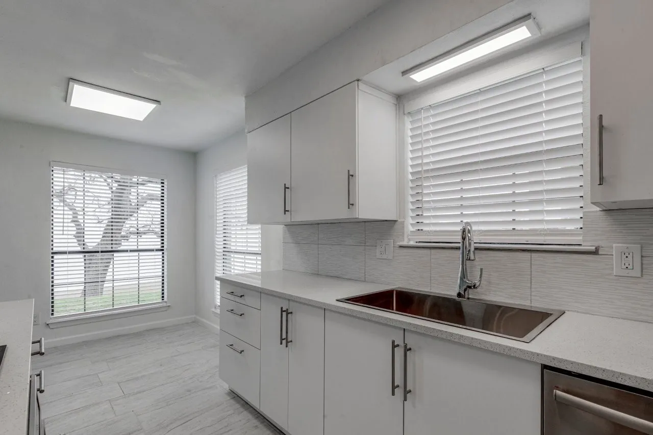 Kitchen with sink, stainless steel dishwasher, white cabinets, and decorative backsplash