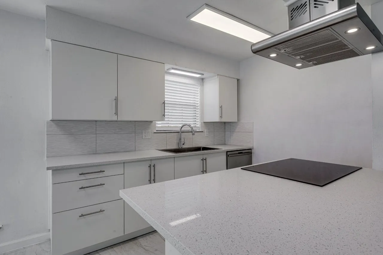 Kitchen with island range hood, dishwasher, sink, white cabinets, and backsplash
