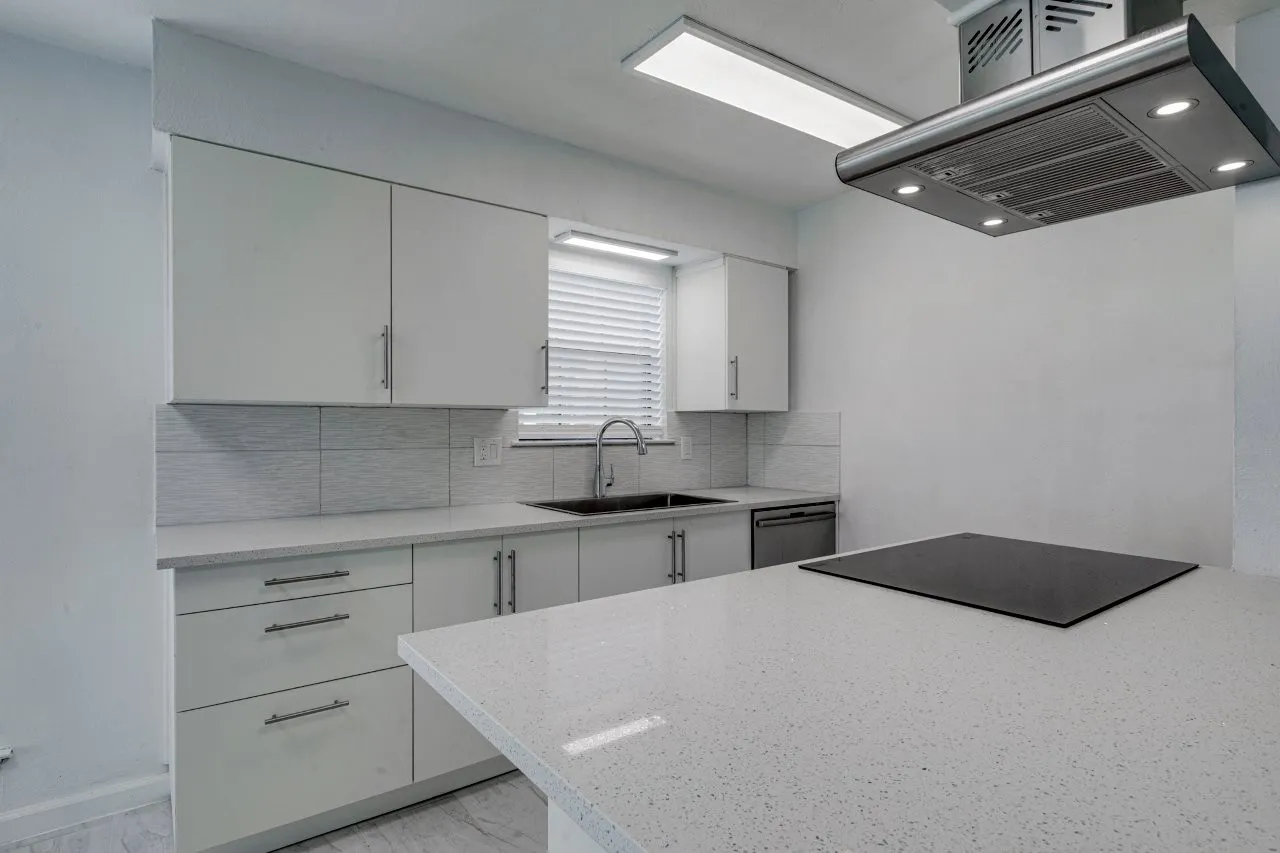 Kitchen with sink, dishwasher, white cabinetry, island exhaust hood, and decorative backsplash
