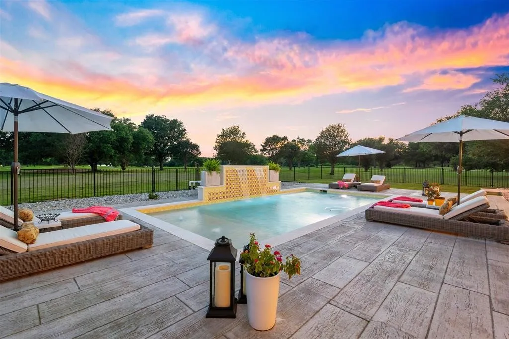 Pool at dusk with pool water feature, outdoor lounge area, a patio, and a lawn