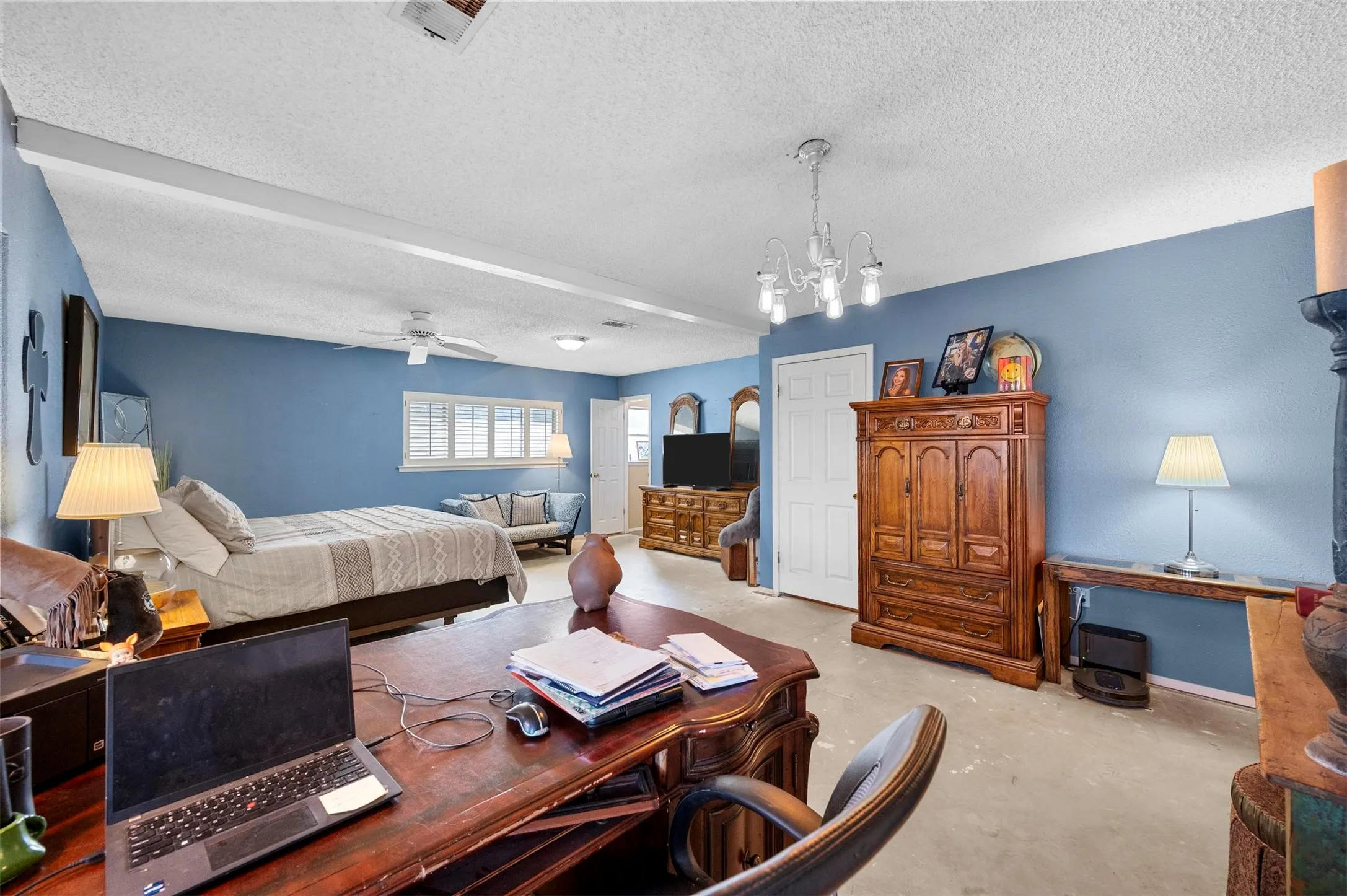 Bedroom with concrete flooring, a textured ceiling, ceiling fan with notable chandelier, and visible vents