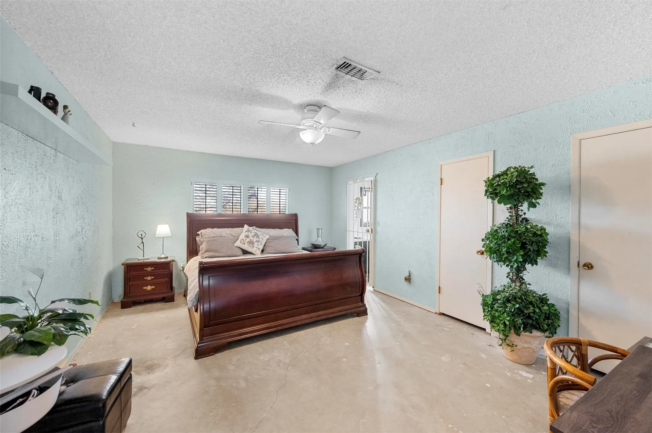 Bedroom featuring a textured ceiling, a textured wall, concrete floors, visible vents, and a ceiling fan
