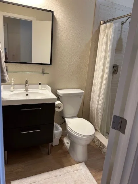 Full bath featuring a textured wall, toilet, wood finished floors, vanity, and a stall shower