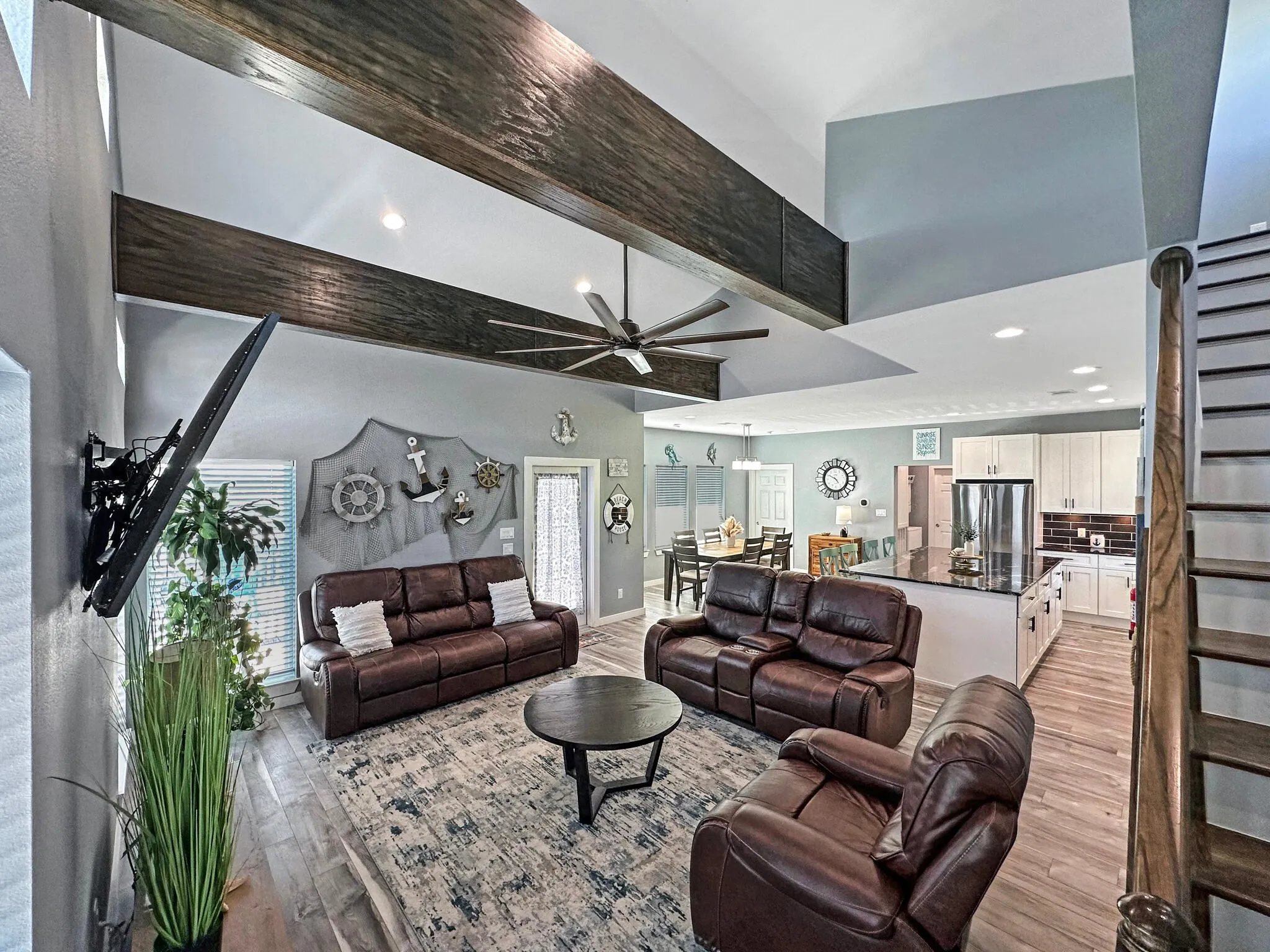 Living area with stairs, ceiling fan, light wood-type flooring, and beam ceiling
