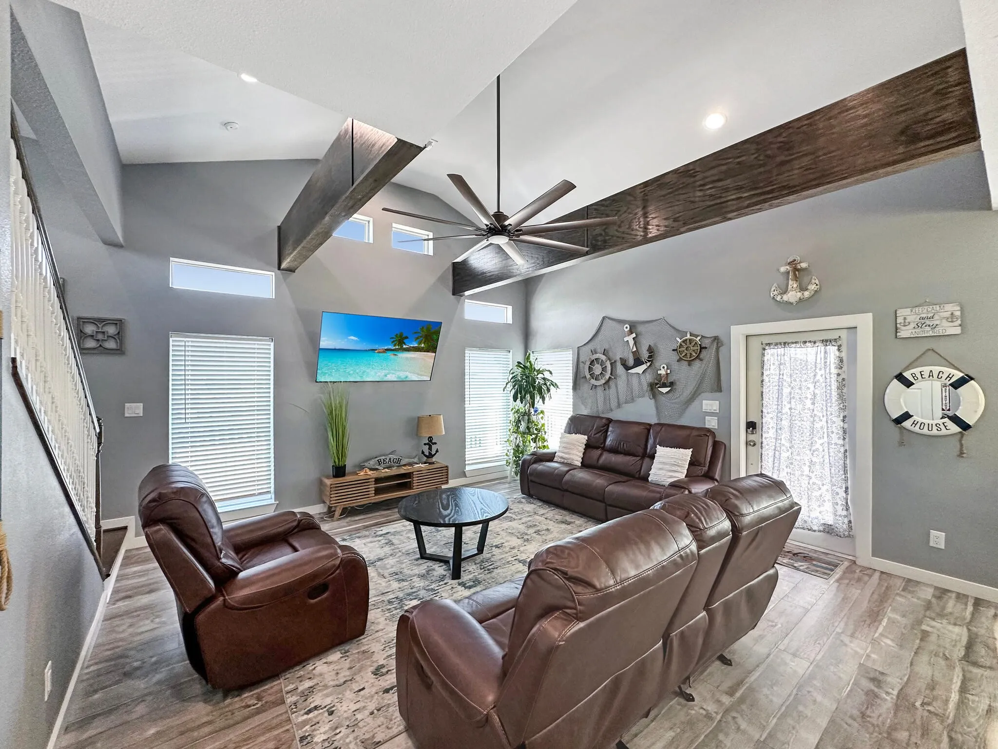 Living room with ceiling fan, a towering ceiling, baseboards, and wood finished floors