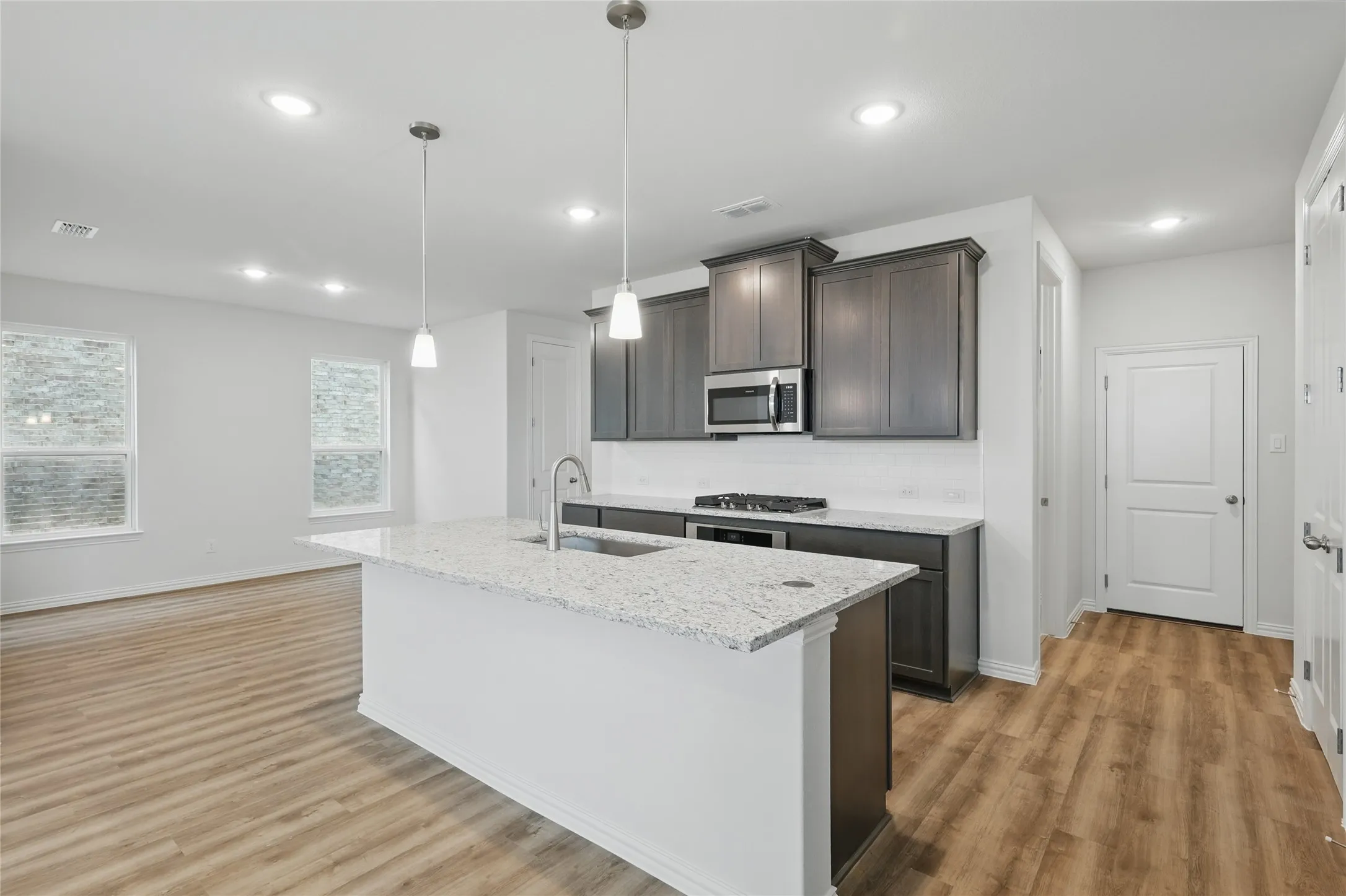 Kitchen featuring light wood finished floors, light stone countertops, pendant lighting, an island with sink, and stainless steel appliances