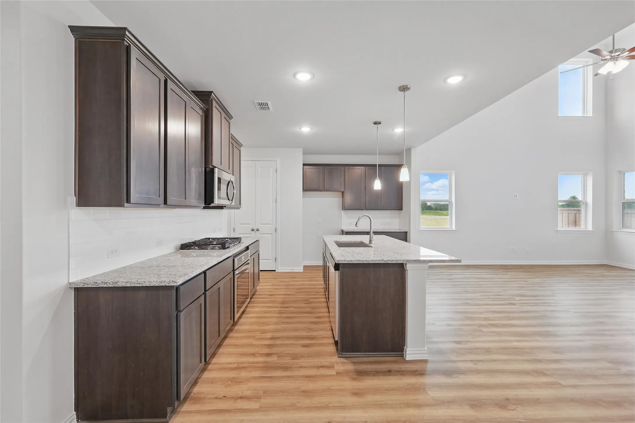 Kitchen featuring dark brown cabinetry, recessed lighting, light wood-style floors, an island with sink, and a towering ceiling