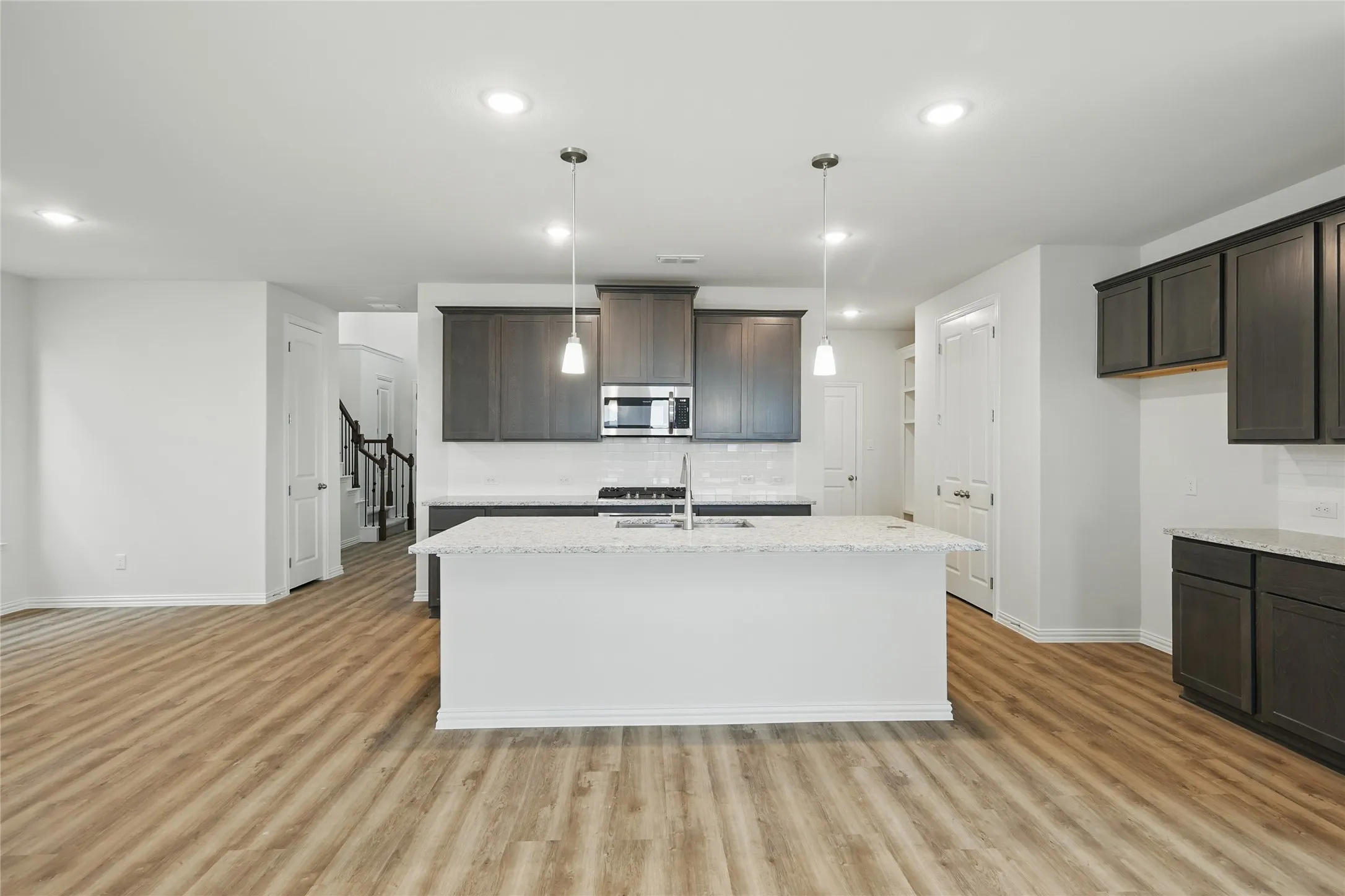 Kitchen with dark brown cabinets, recessed lighting, light wood-type flooring, a center island with sink, and stainless steel microwave