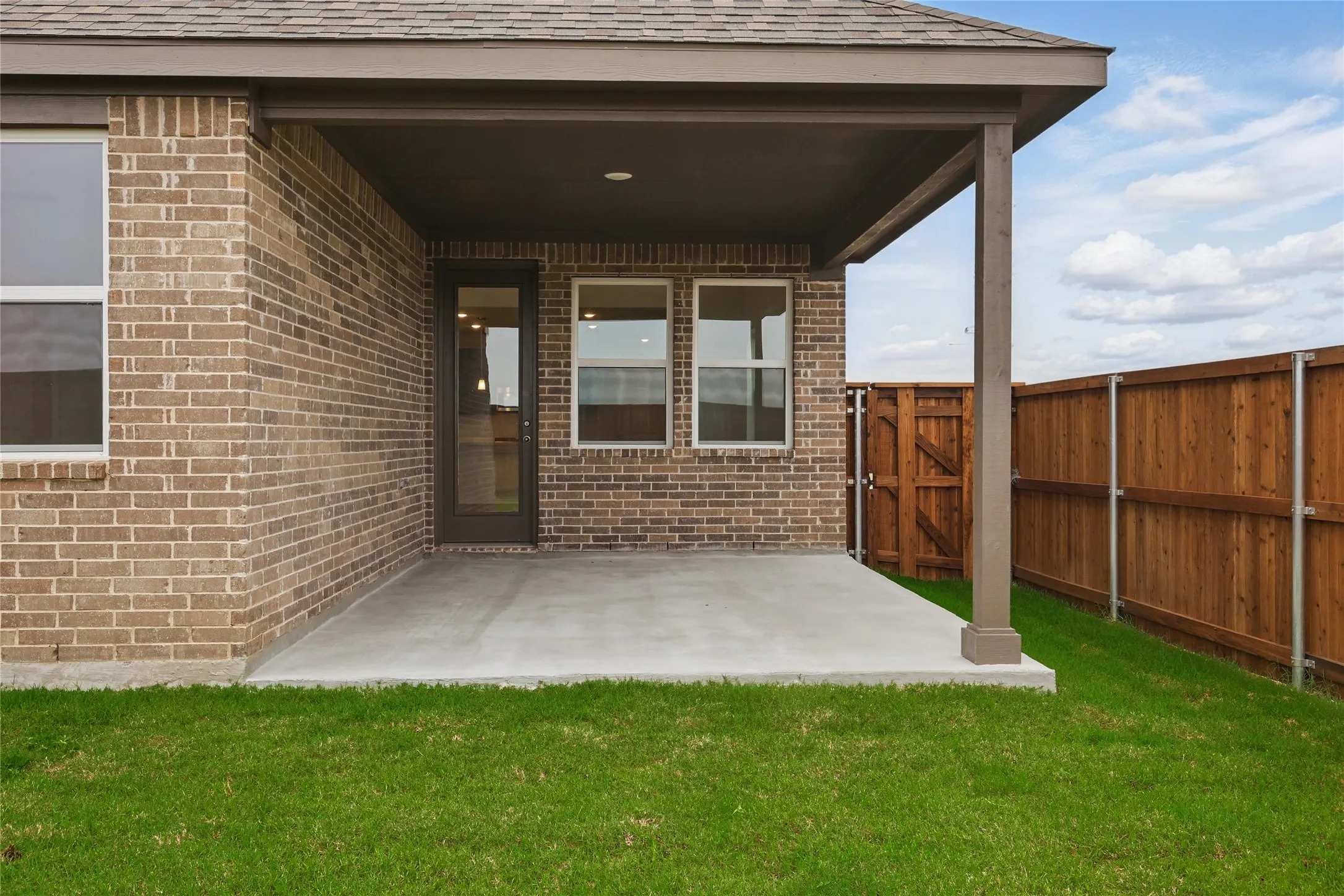 View of exterior entry with a patio, brick siding, and roof with shingles