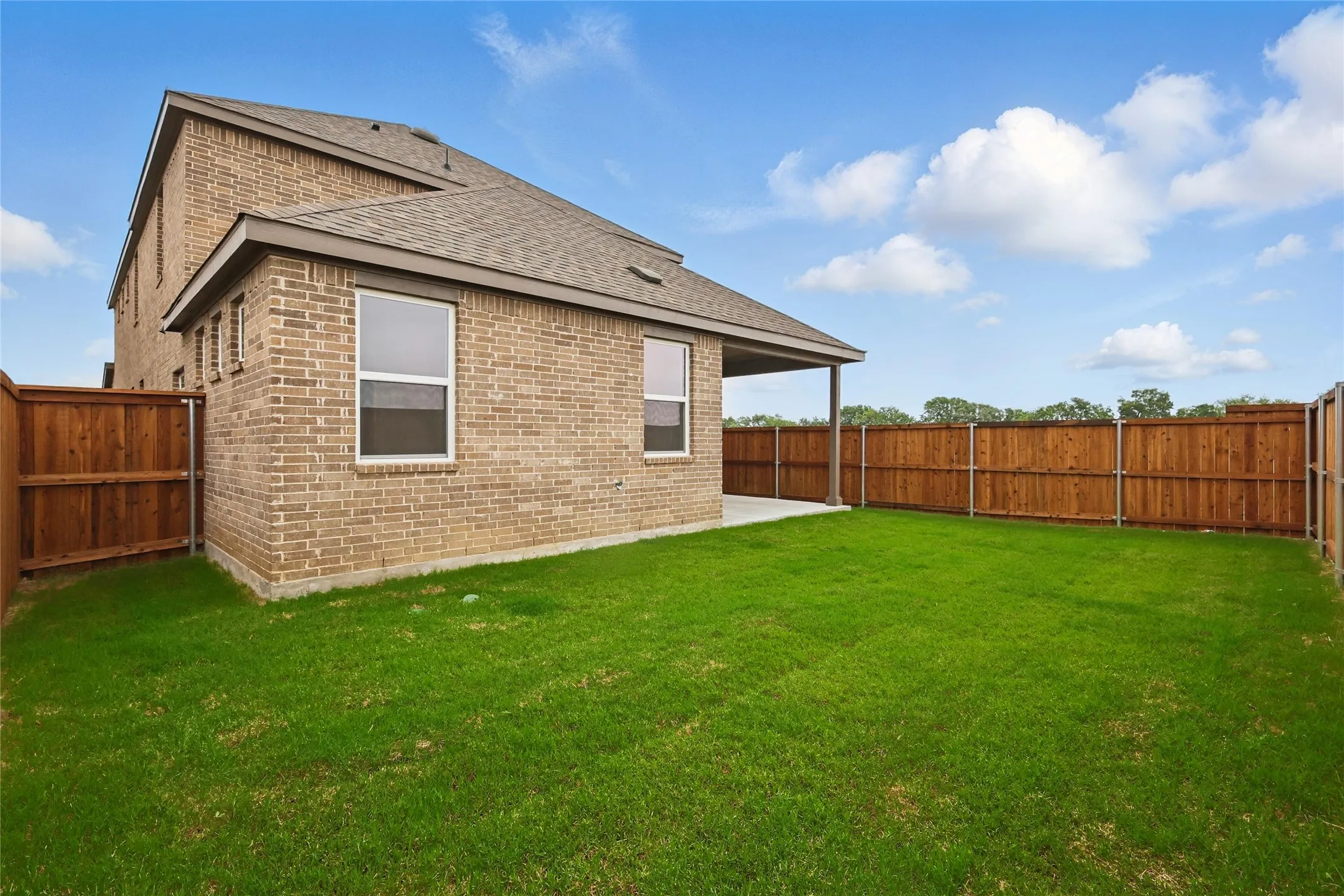 Back of property featuring roof with shingles, brick siding, a fenced backyard, and a patio area
