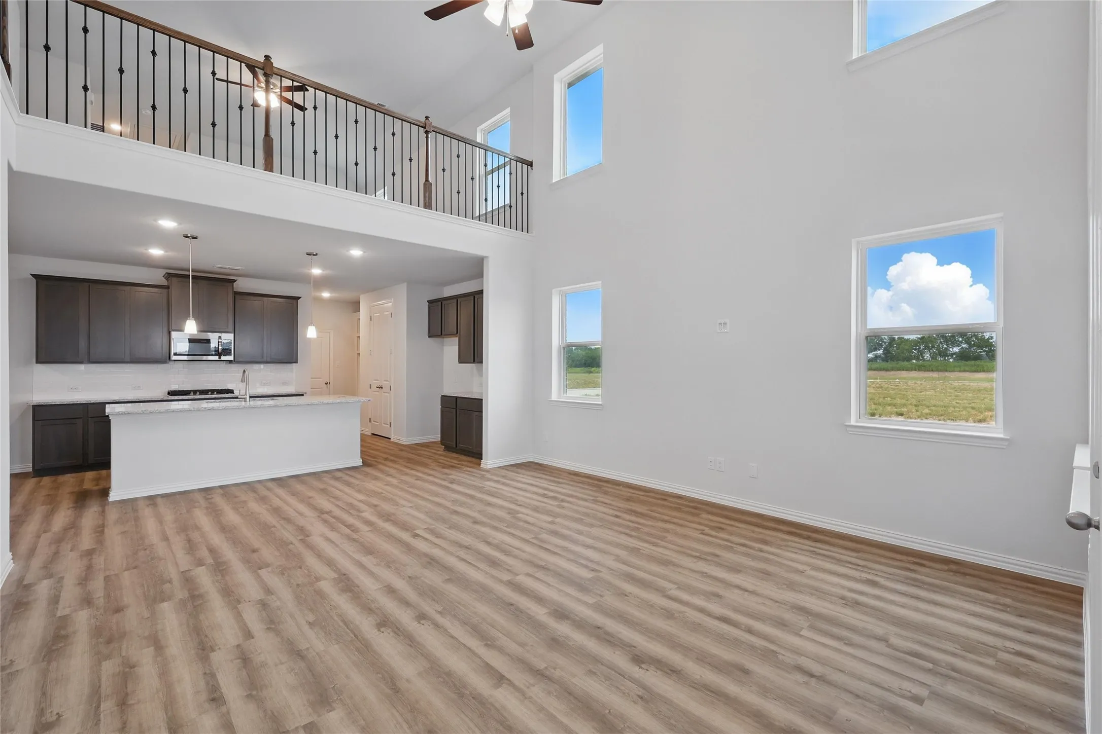 Unfurnished living room featuring a ceiling fan, plenty of natural light, a high ceiling, and light wood-style floors