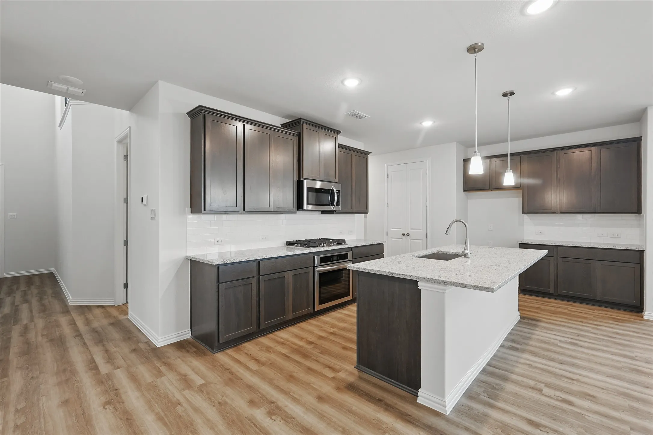 Kitchen with dark brown cabinetry, tasteful backsplash, light wood finished floors, light stone counters, and appliances with stainless steel finishes