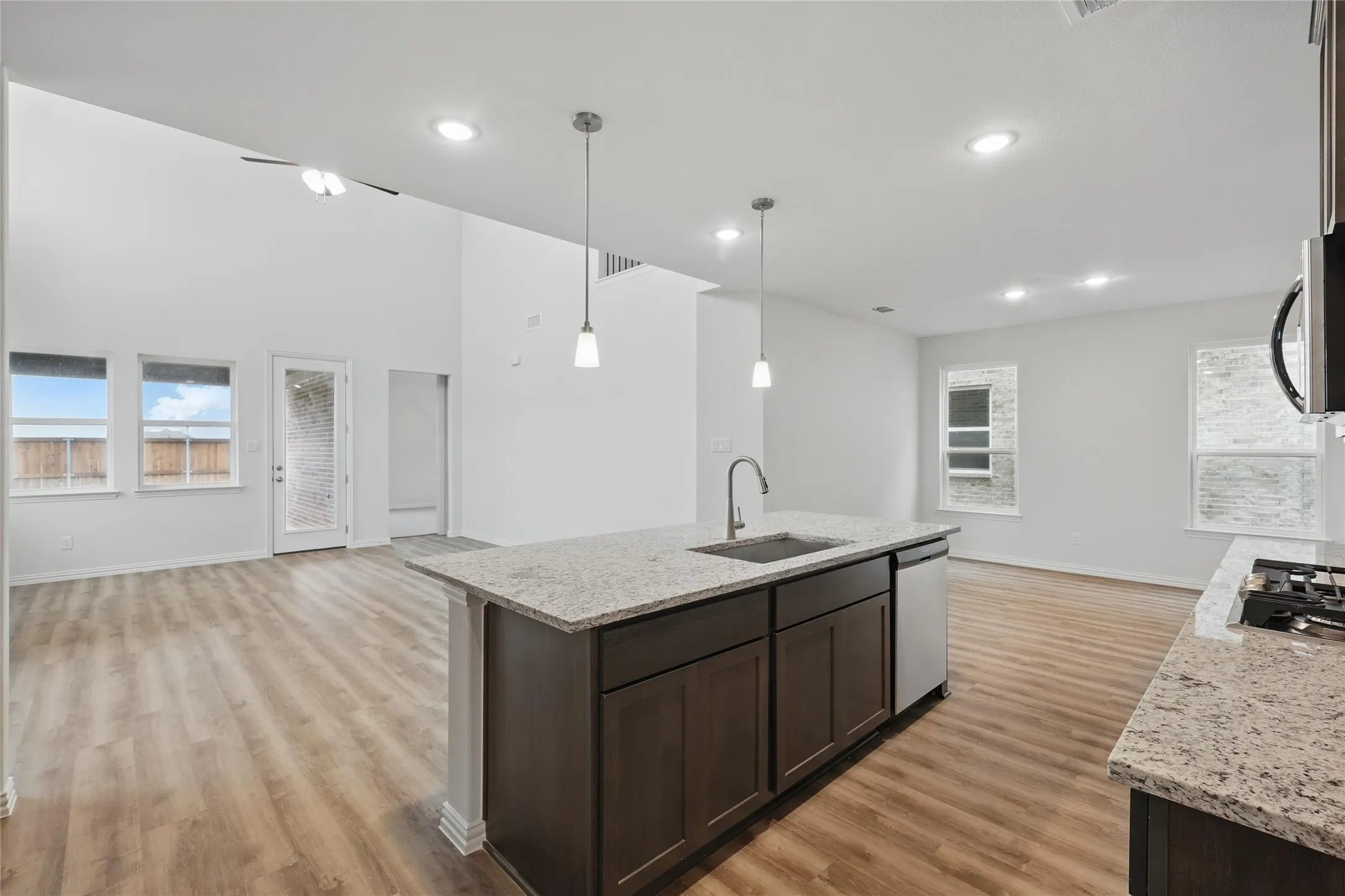 Kitchen with open floor plan, dark brown cabinetry, light wood-type flooring, appliances with stainless steel finishes, and light stone counters