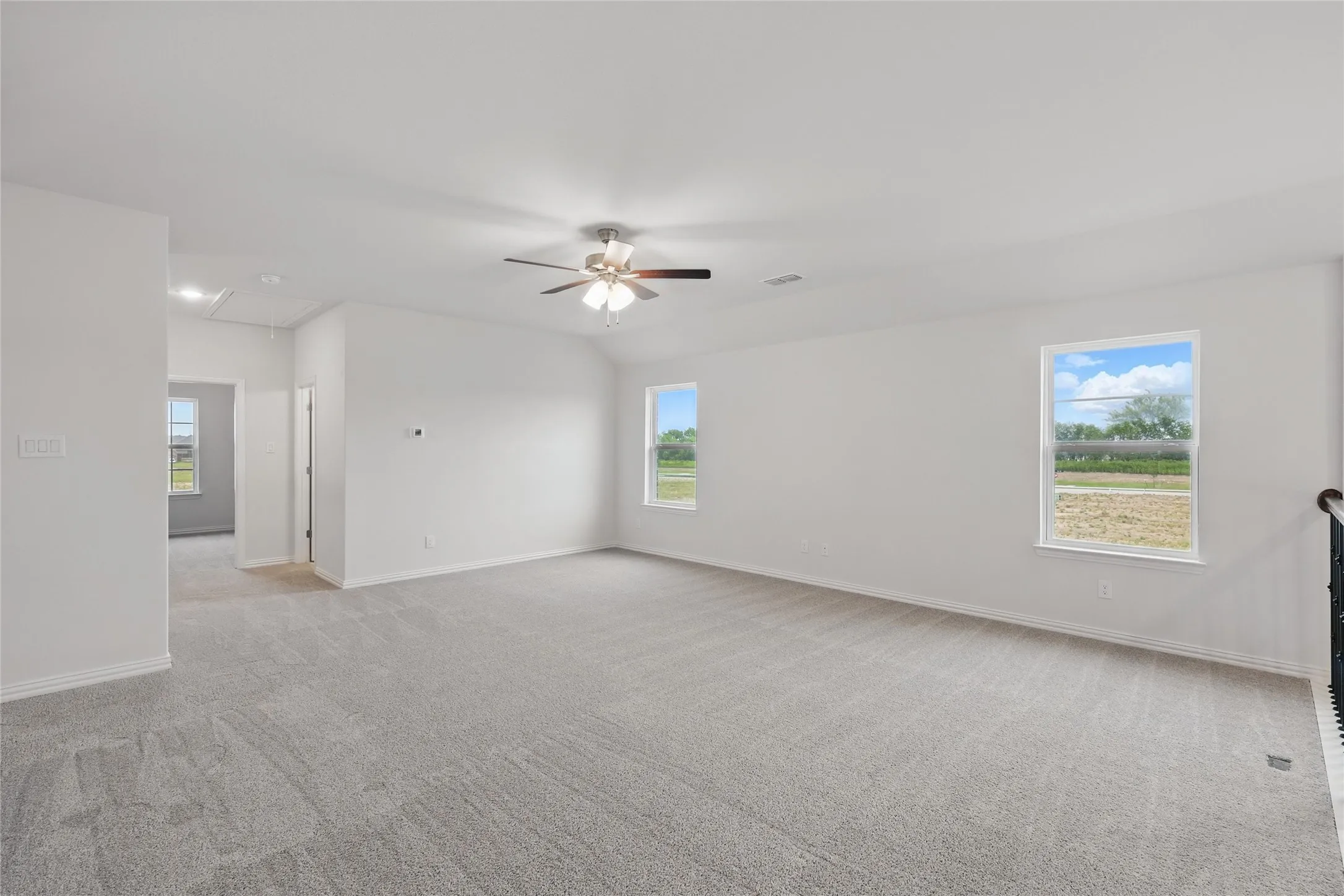 Unfurnished room with attic access, healthy amount of natural light, light colored carpet, and lofted ceiling