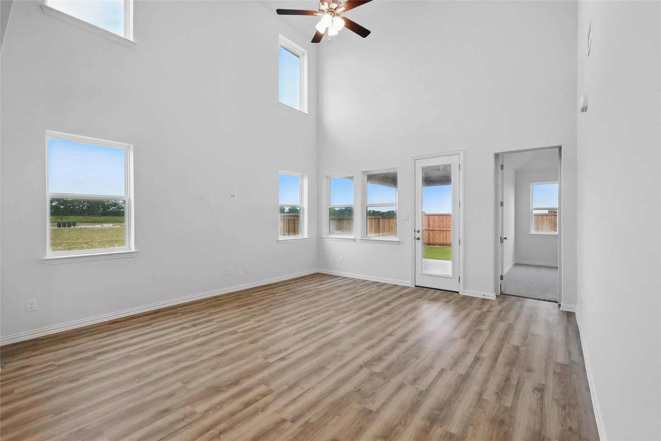 Empty room with a towering ceiling, light wood-style flooring, and ceiling fan