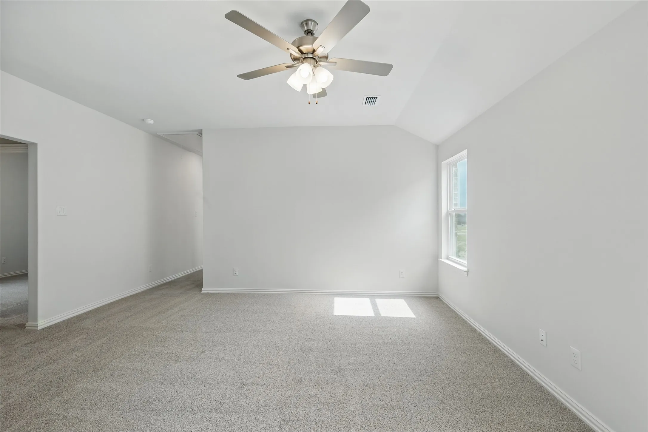 Unfurnished room featuring light colored carpet, vaulted ceiling, and a ceiling fan