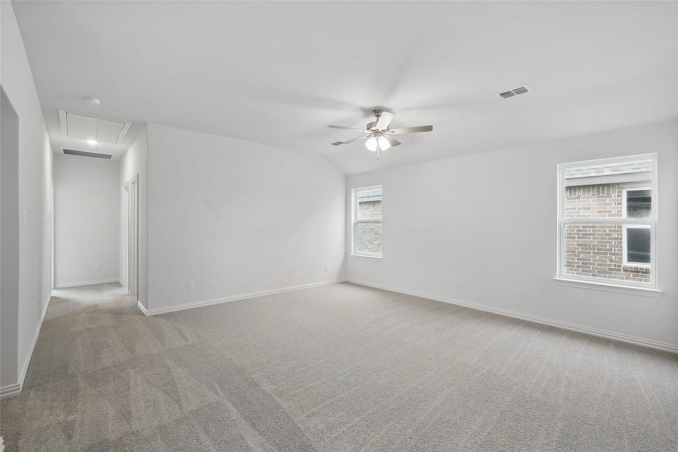 Spare room featuring attic access, light colored carpet, a ceiling fan, and lofted ceiling