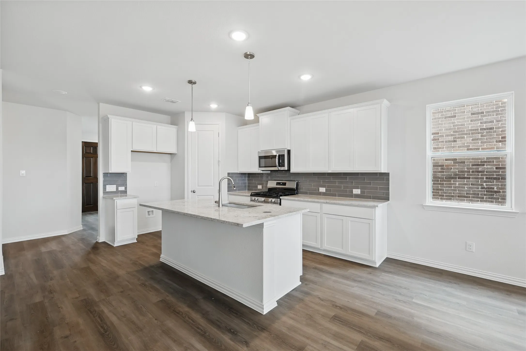 Kitchen featuring hanging light fixtures, decorative backsplash, dark wood-style floors, white cabinets, and light stone counters