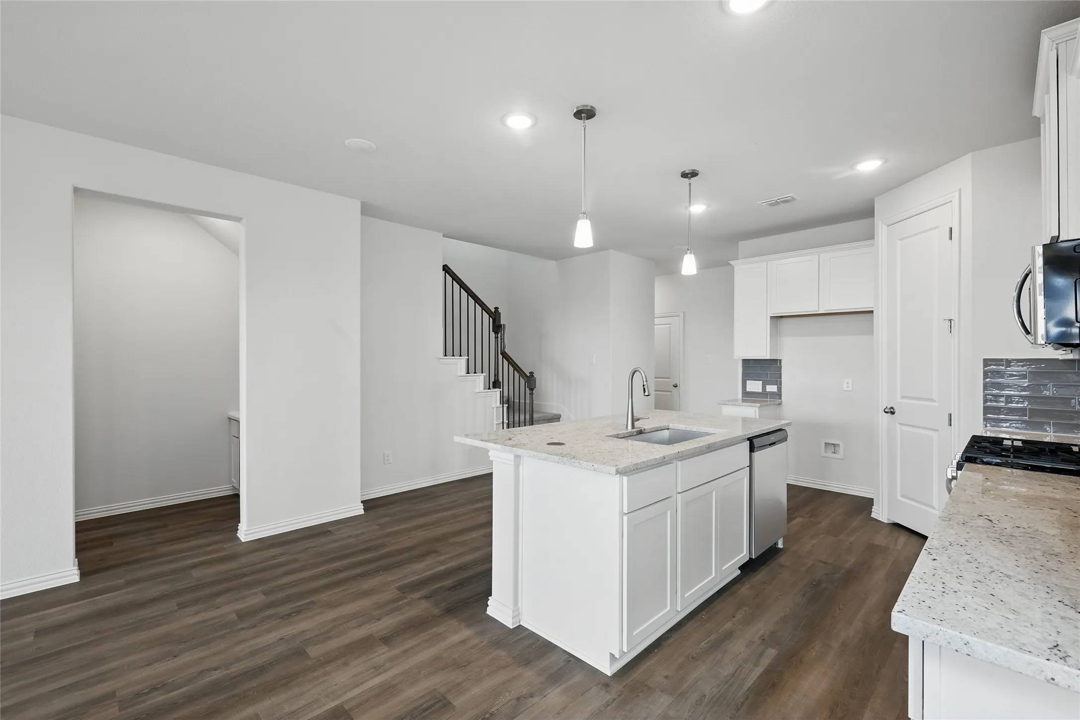 Kitchen featuring dark wood-style floors, light stone counters, recessed lighting, a center island with sink, and appliances with stainless steel finishes