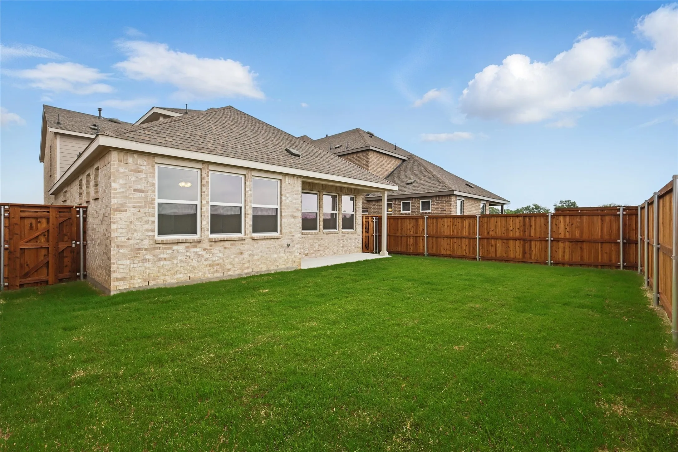 Rear view of property featuring a patio area, brick siding, roof with shingles, a fenced backyard, and a gate