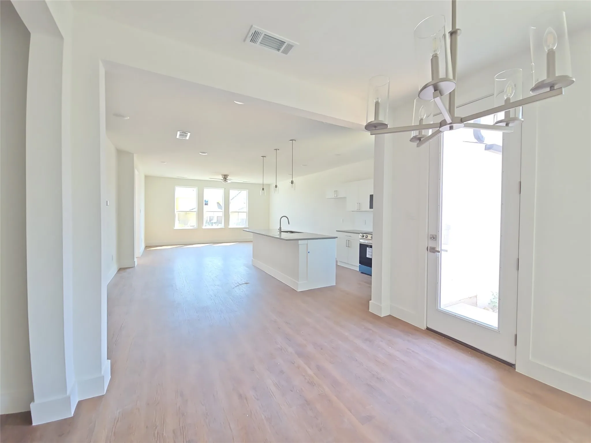 Expansive open-concept living area featuring wood-finish flooring, a kitchen island with sink, and white cabinetry