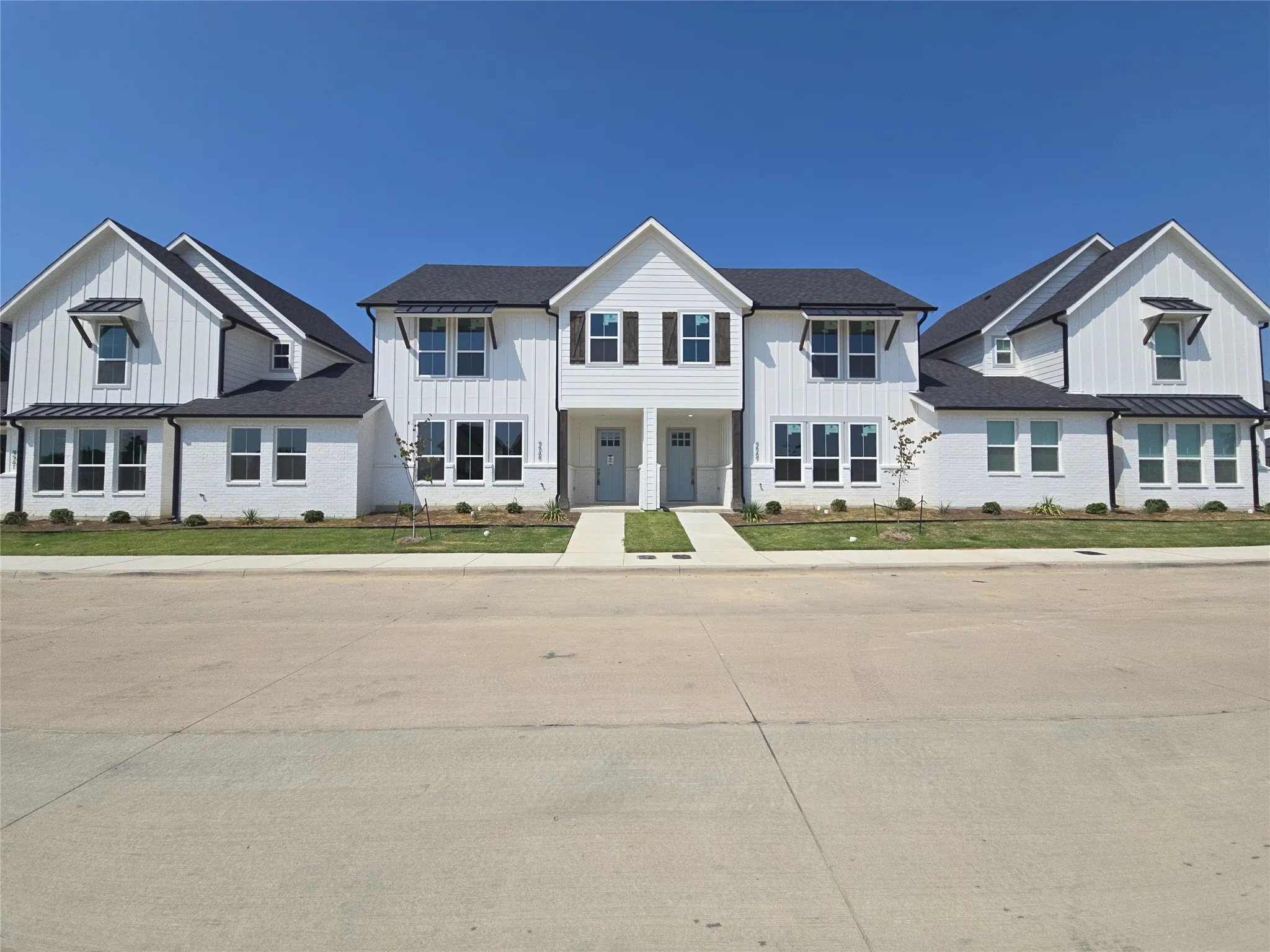 White brick and vertical siding exterior with black gabled roofs, multiple windows, and a paved walkway