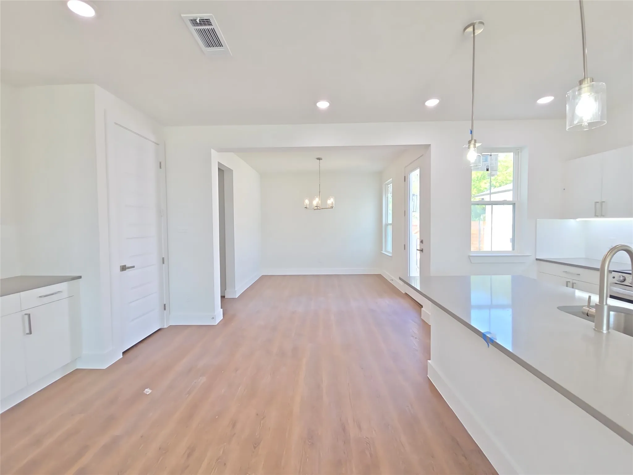 Open-concept living area with wood-finish flooring, recessed lighting, and a kitchen island featuring a stainless steel sink and gooseneck faucet