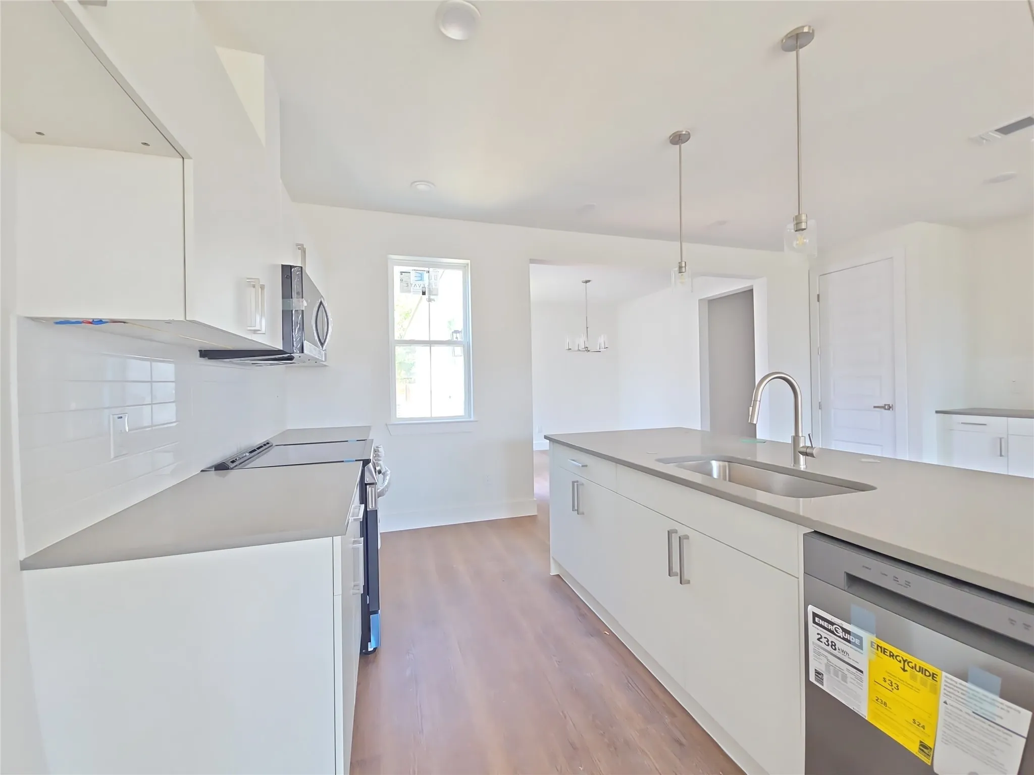 Contemporary kitchen featuring an island with an undermount sink, pendant lighting, wood-finish flooring, white cabinetry, and stainless steel appliances