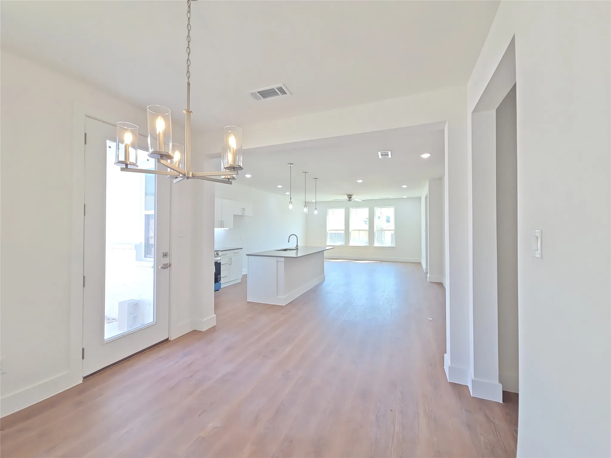 Open-concept living space with wood-finish flooring, a contemporary chandelier, a kitchen island with an undermount sink, and recessed lighting