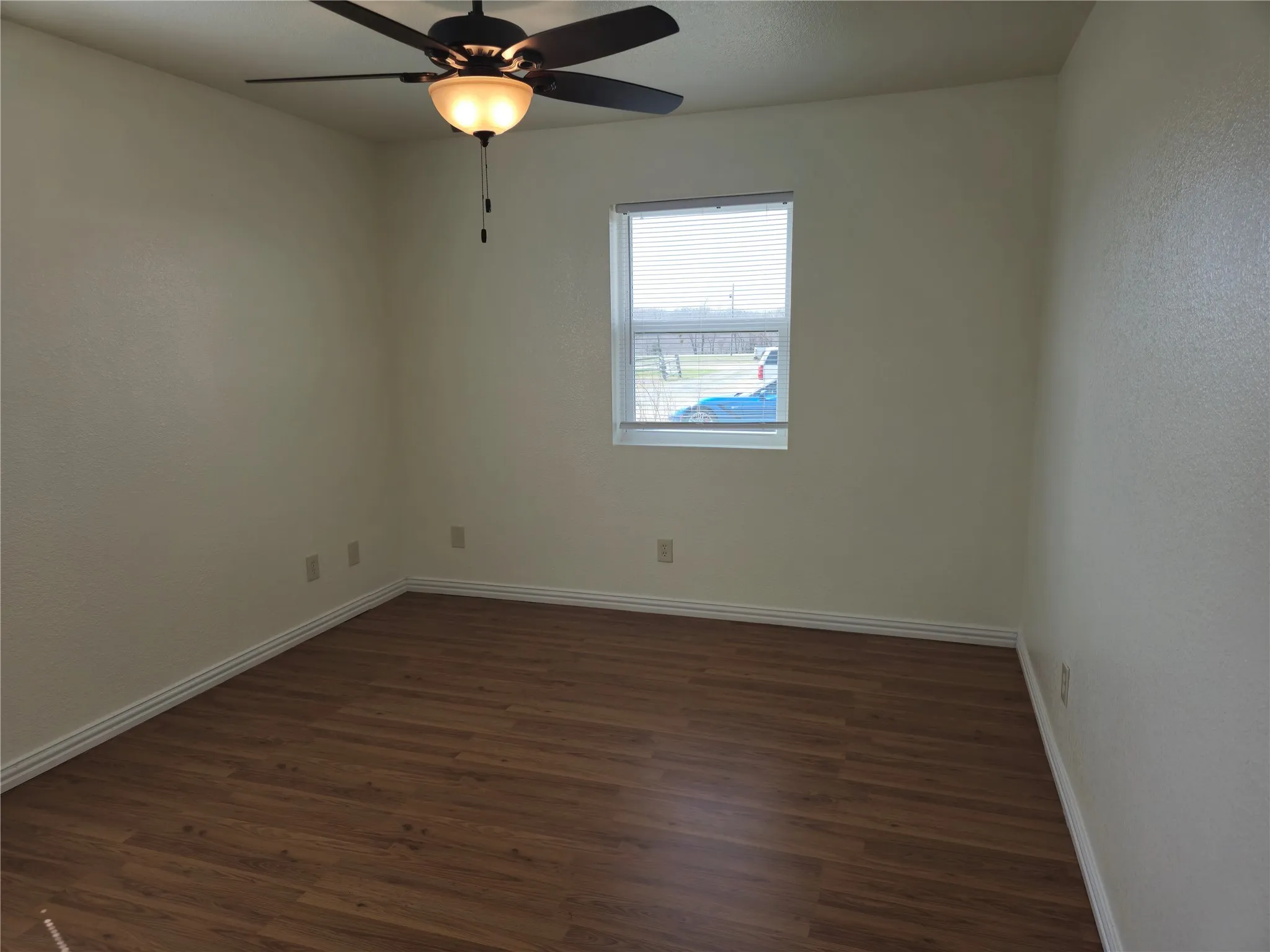 Empty room with dark wood finished floors, a ceiling fan, and baseboards