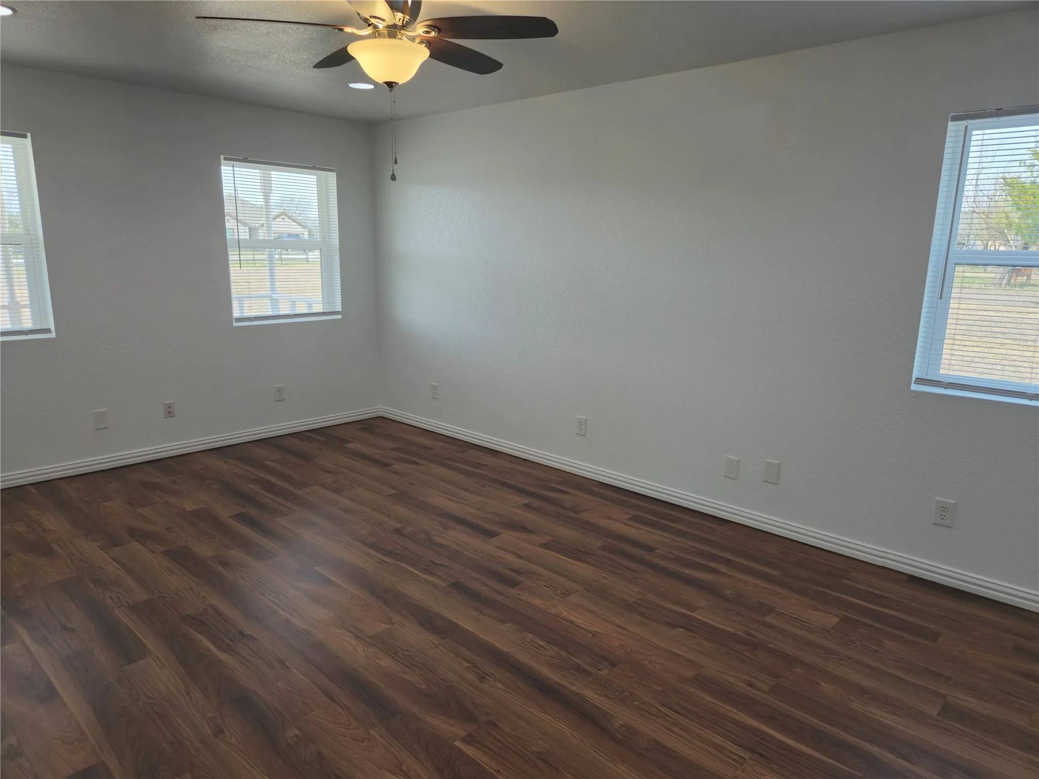 Spare room featuring plenty of natural light, a ceiling fan, dark wood-type flooring, and baseboards