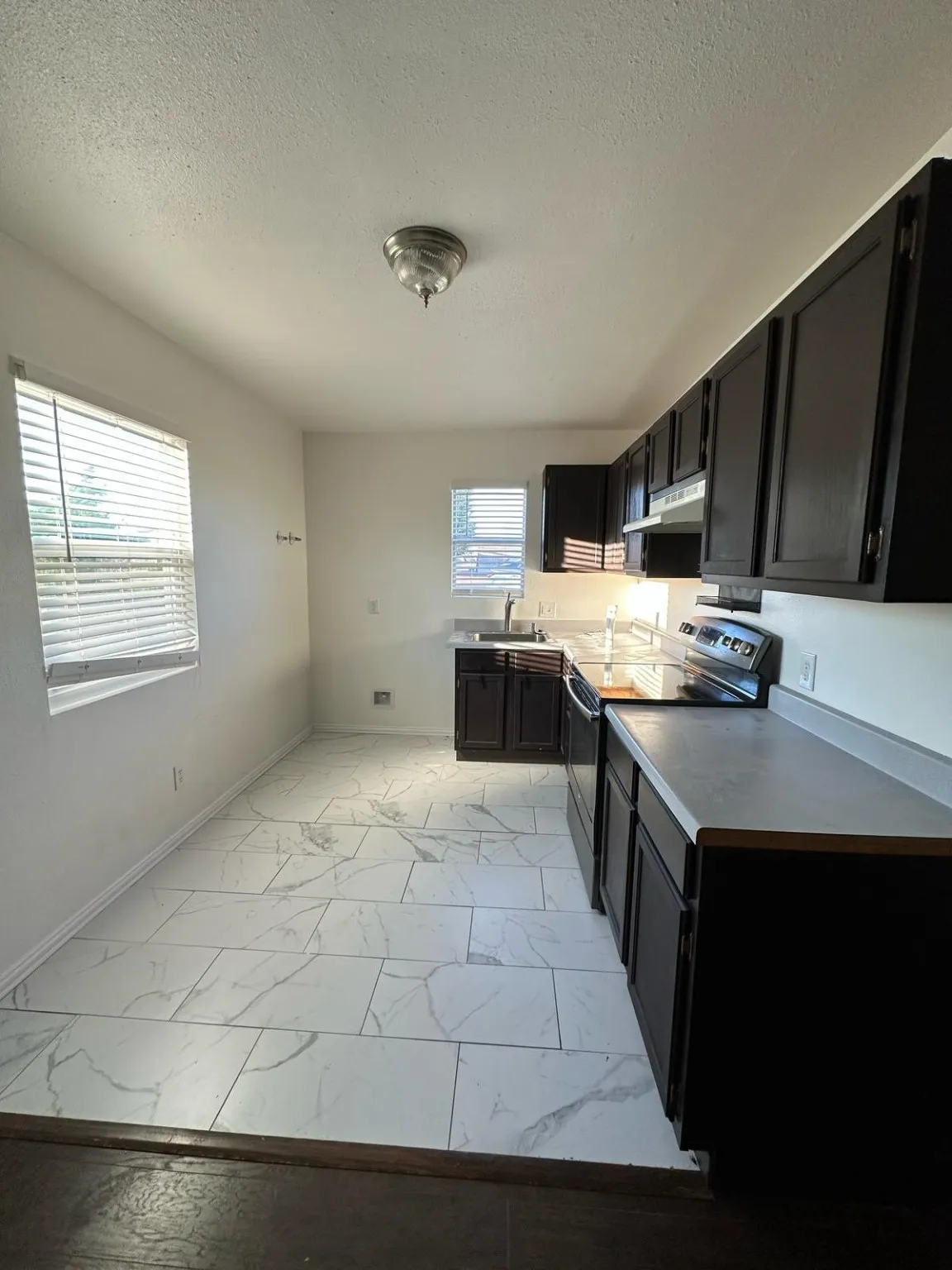  Barndo Kitchen featuring black electric range, light marble finish floors, dark cabinetry, a textured ceiling, and light countertops