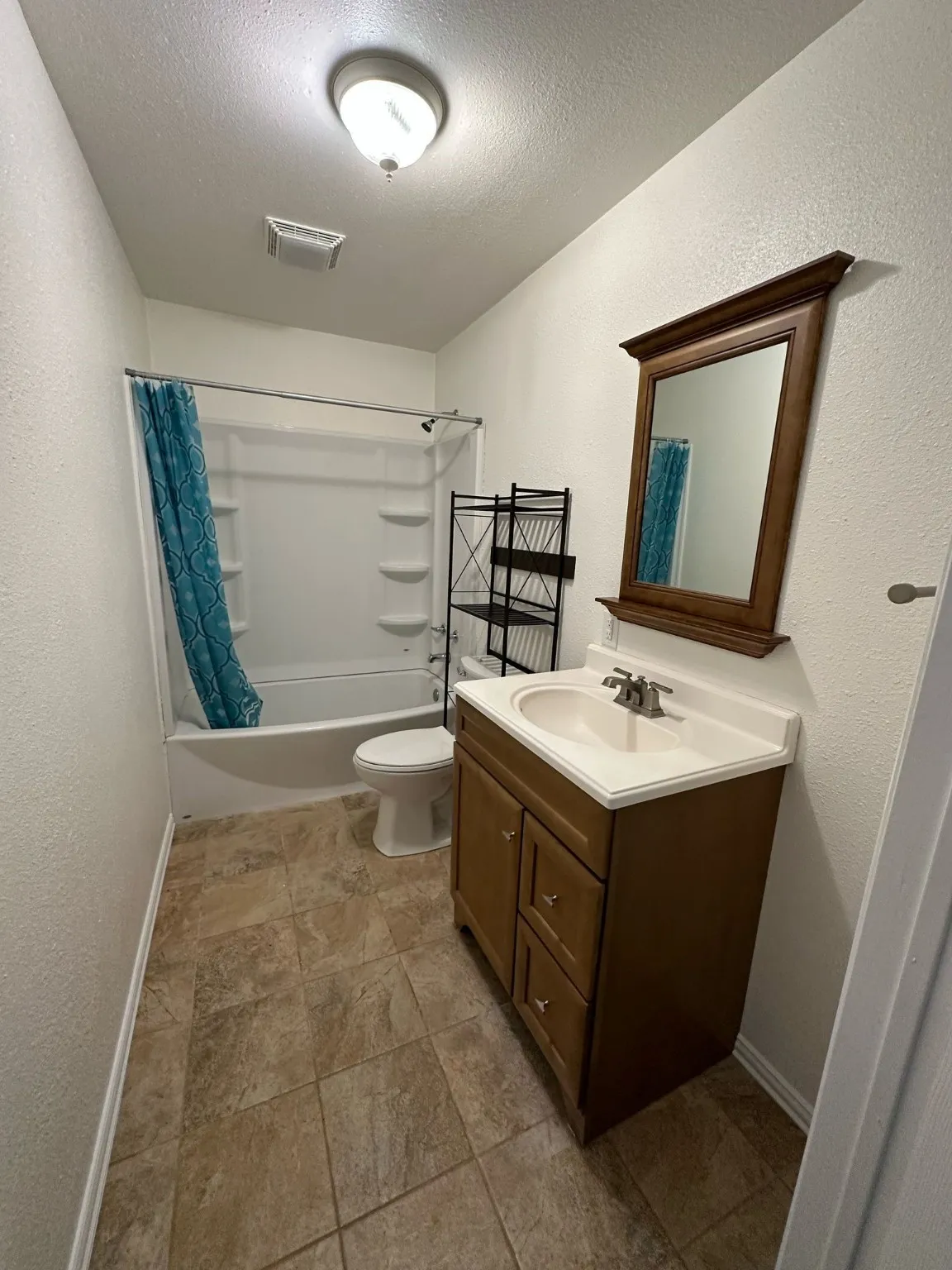 Bathroom with a textured wall, shower / tub combo, vanity, and a textured ceiling