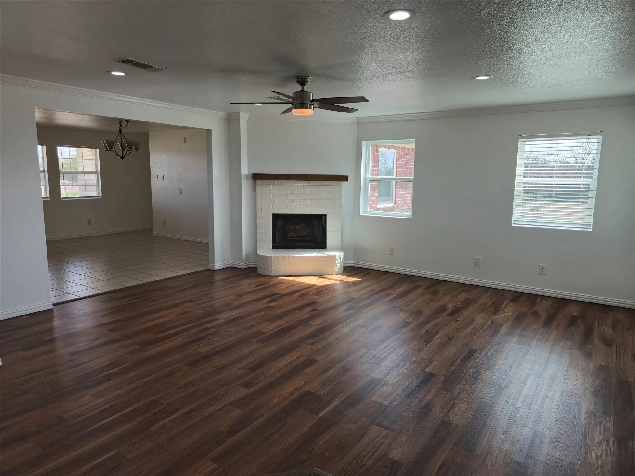 Unfurnished living room featuring visible vents, dark wood-type flooring, ornamental molding, a textured ceiling, and a brick fireplace