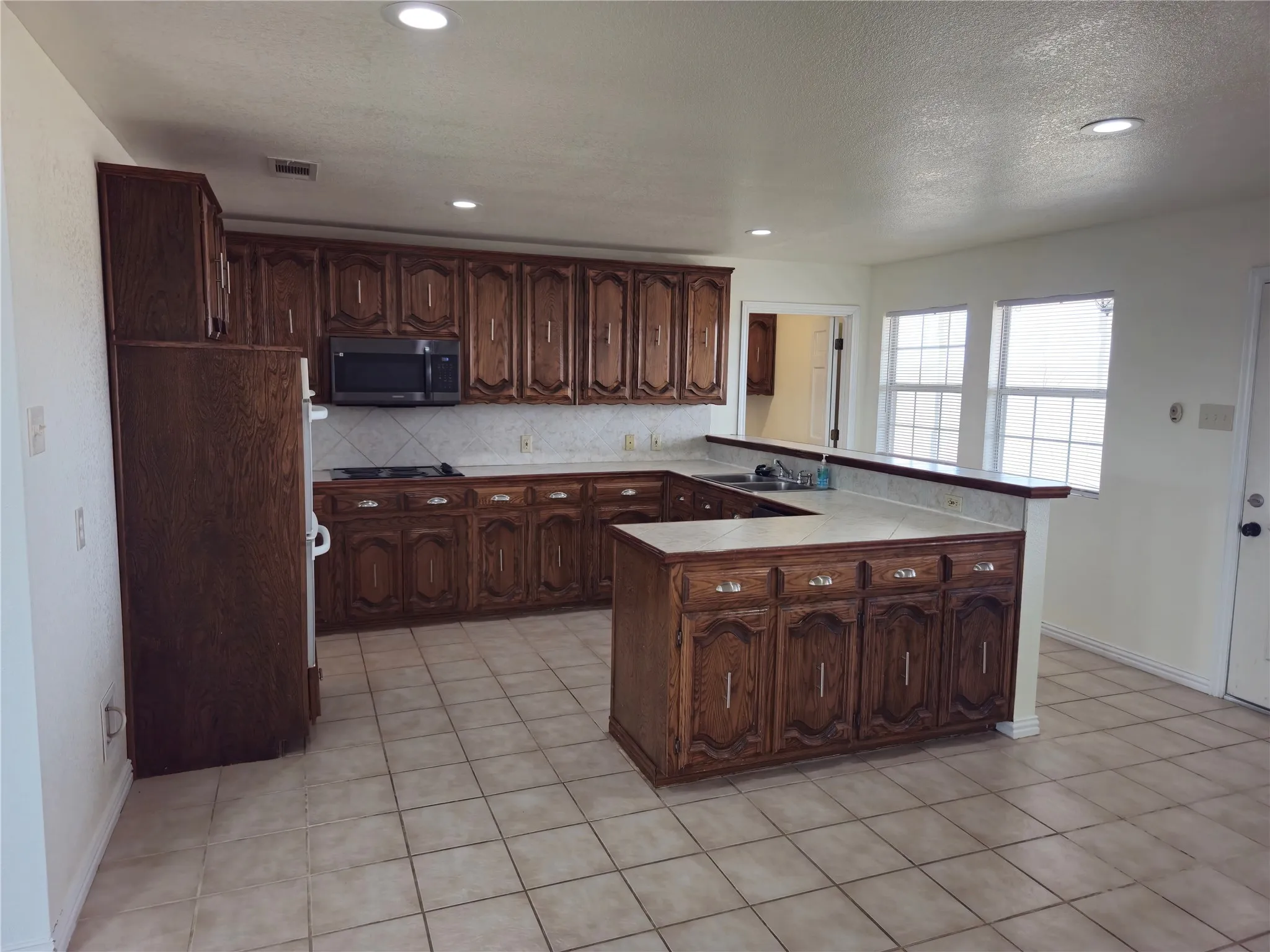 Kitchen with visible vents, stainless steel microwave, tasteful backsplash, a peninsula, and black electric cooktop