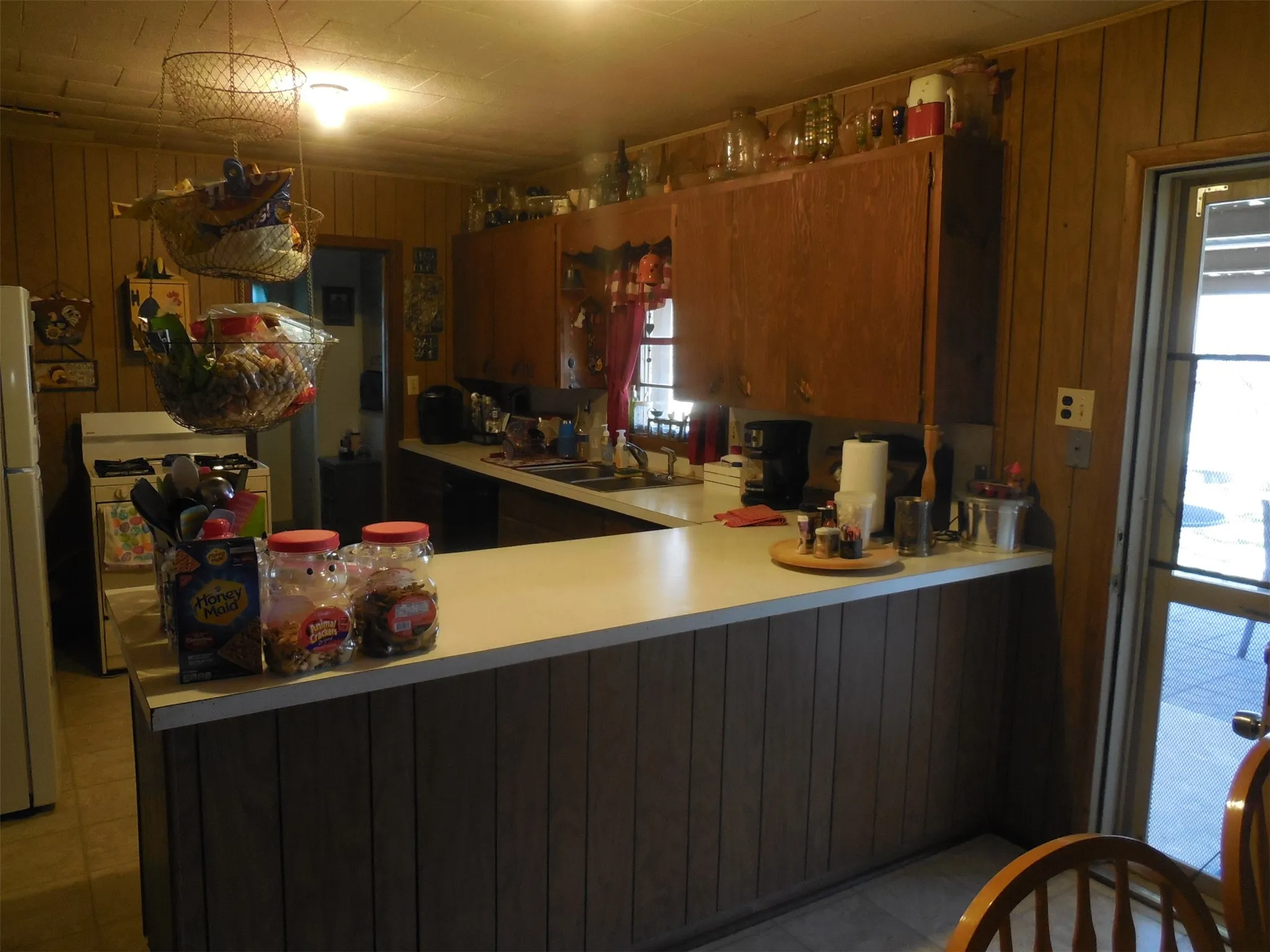 Kitchen featuring wooden walls, light countertops, brown cabinetry, white appliances, and a sink