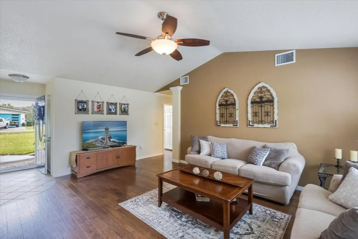 Living area with lofted ceiling, visible vents, ornate columns, and wood finished floors